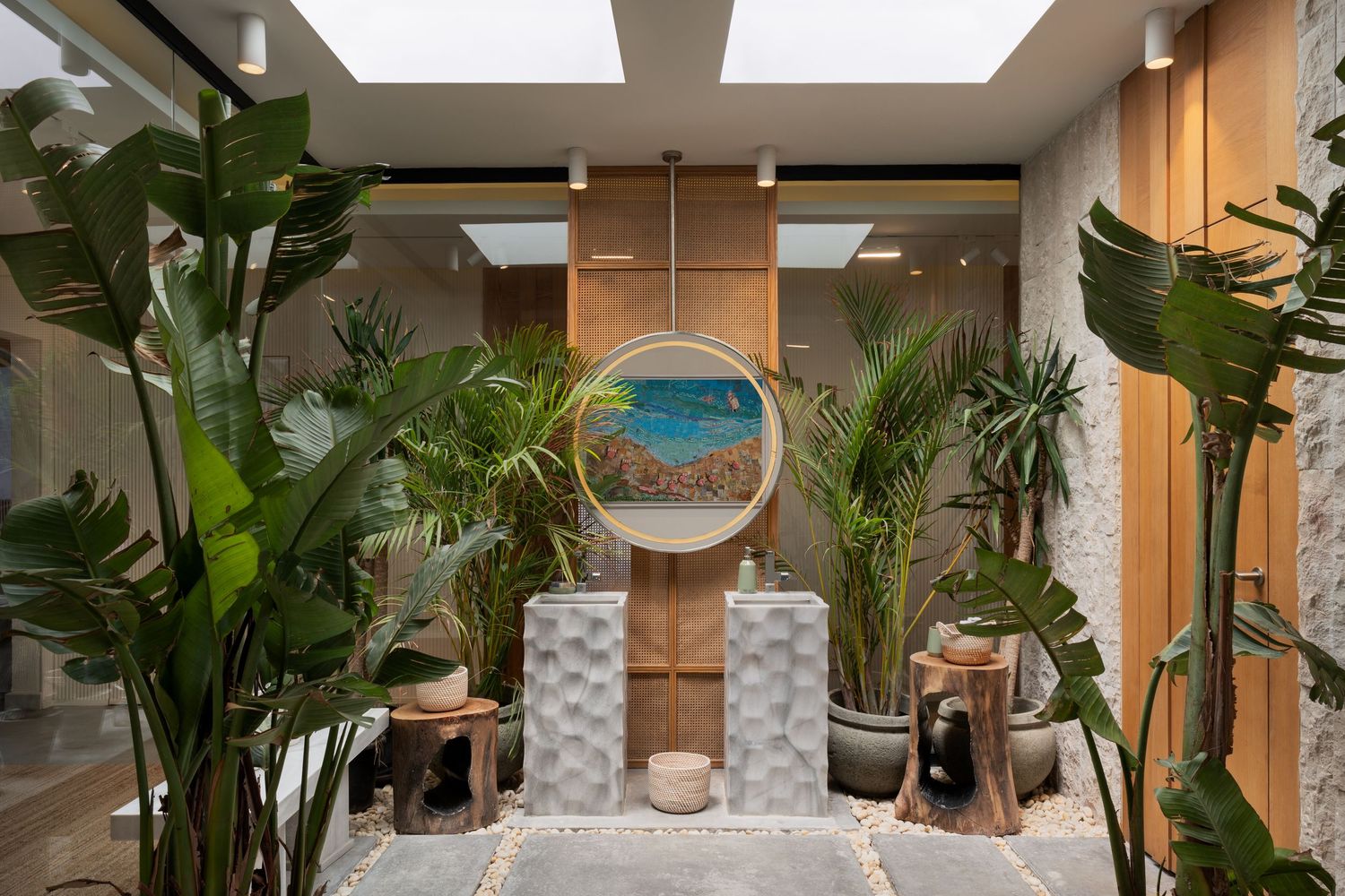 Lush indoor garden atrium with tropical plants, circular mirror artwork, bamboo accents, and natural skylight overhead.