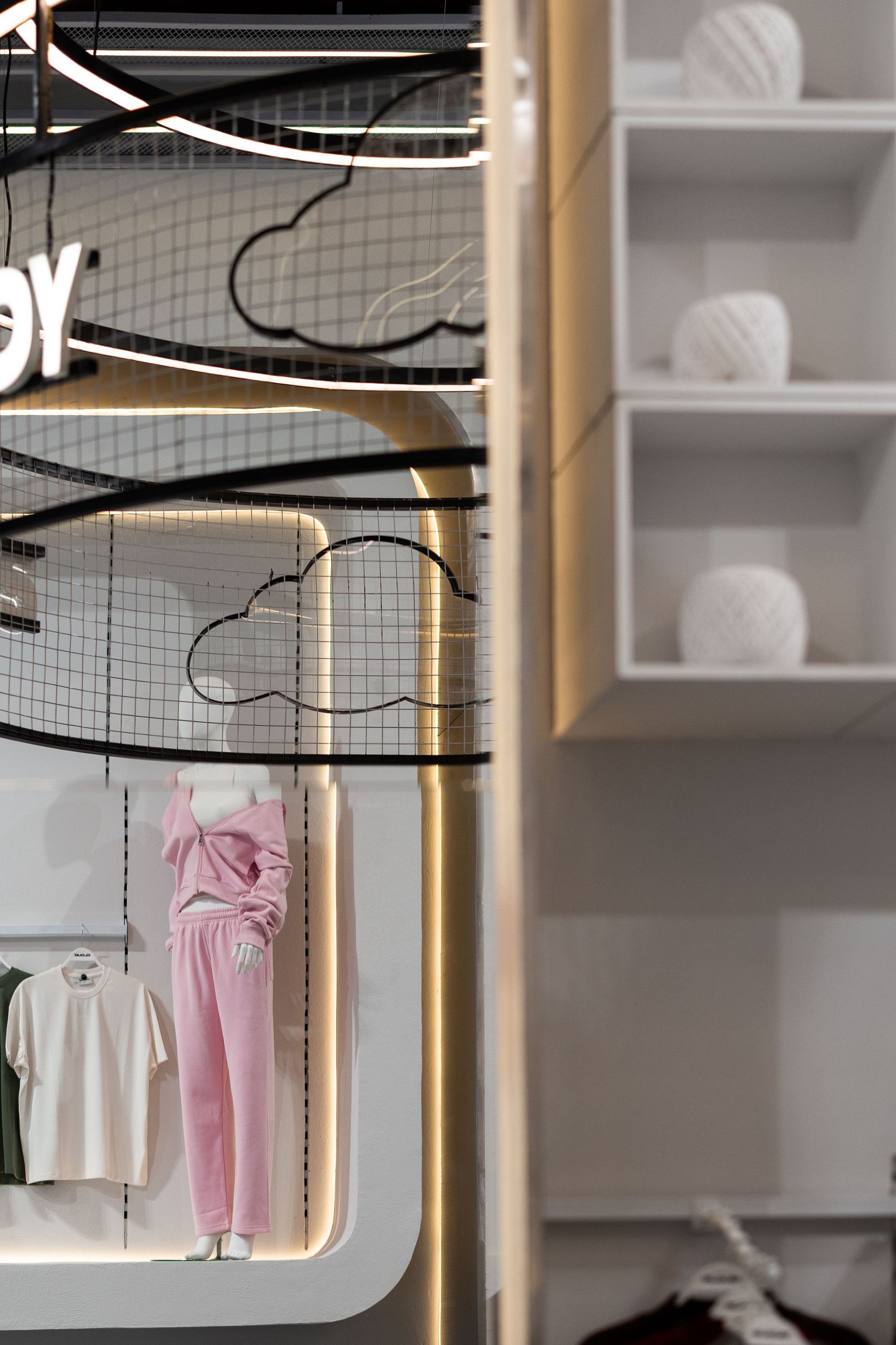 Pink outfit on mannequin displayed in illuminated boutique with cloud motifs and yarn ball decor.