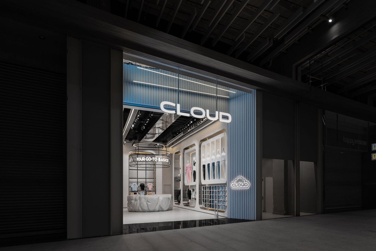 Cloud retail store exterior at night with illuminated signage, visible through a dark industrial exhibition hall entrance.