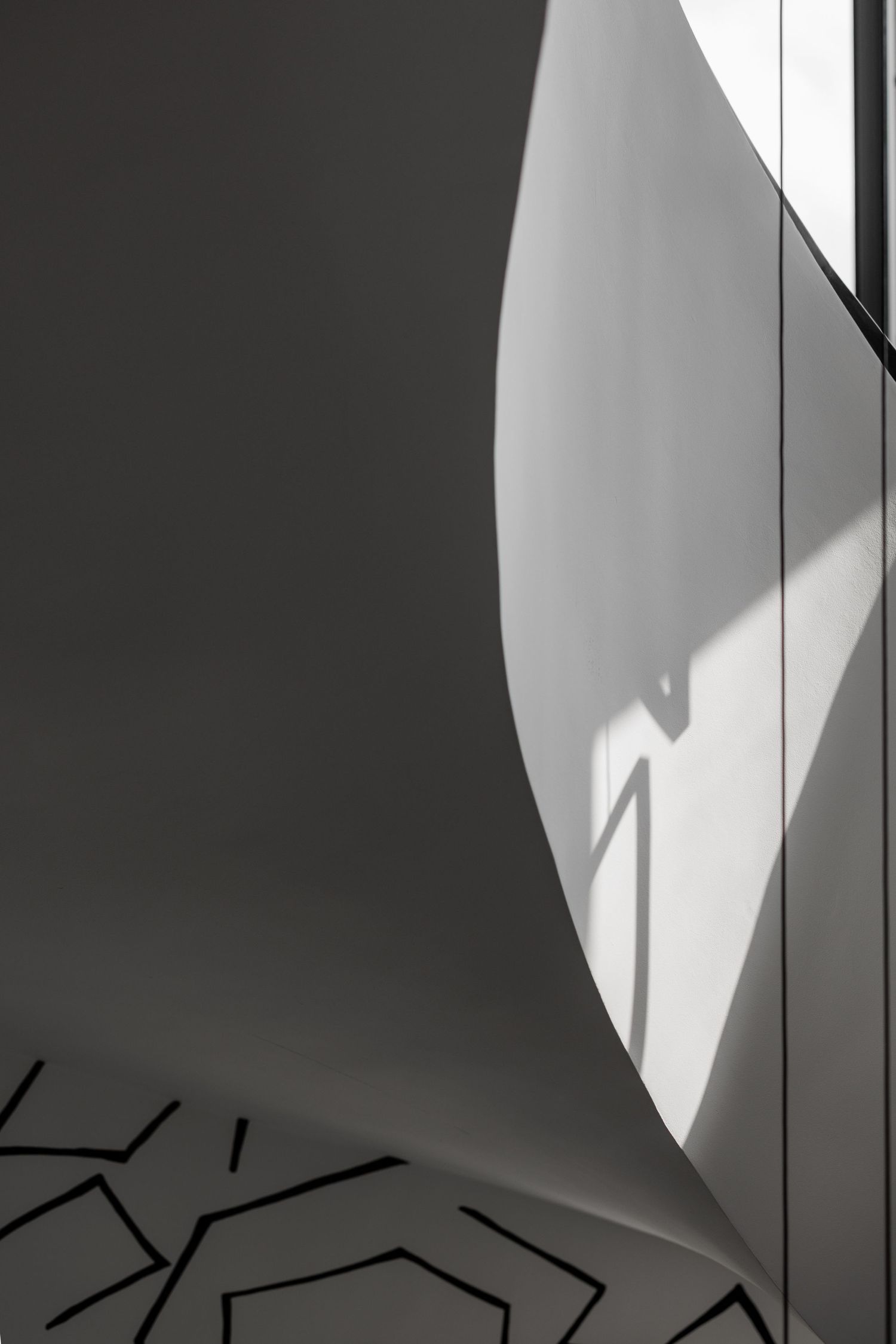 Dramatic curved white wall with shadow play and geometric black line pattern at base.