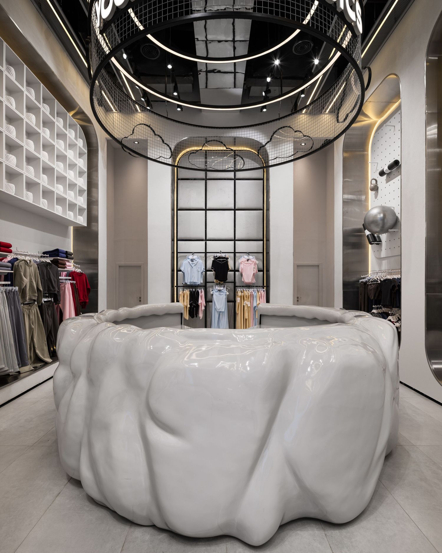 Luxury fashion boutique with large white sculptural center display, circular ceiling feature, and clothing racks around perimeter.