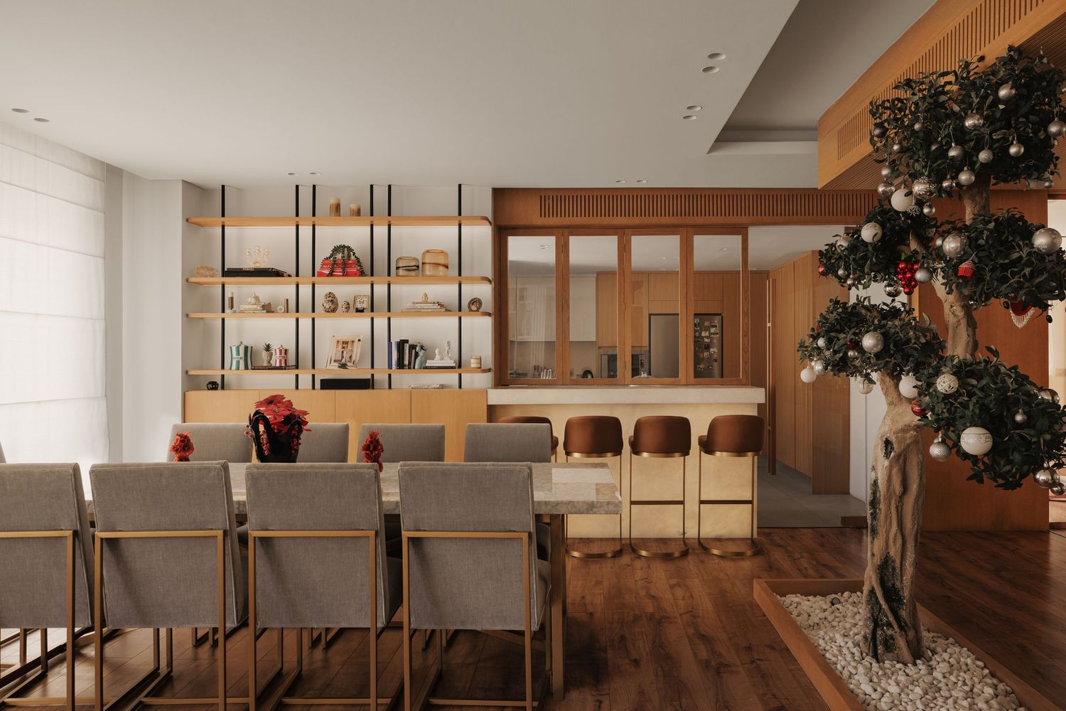 Modern dining room with gray upholstered chairs, wooden shelving, and a decorated Christmas tree in warm interior.