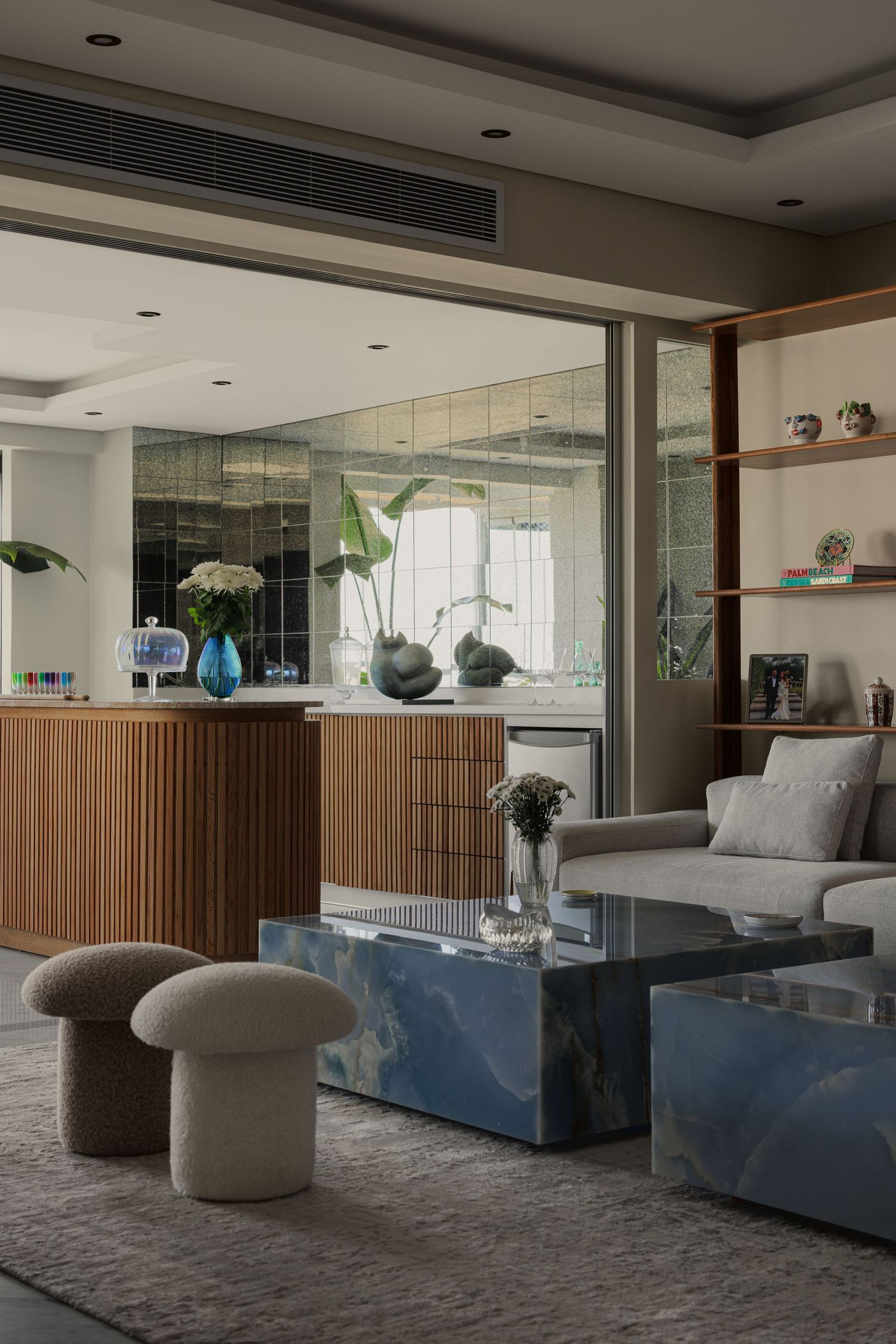 Contemporary living room with fluted wood bar, gray sofa, blue marble coffee table, and mirrored wall accents.
