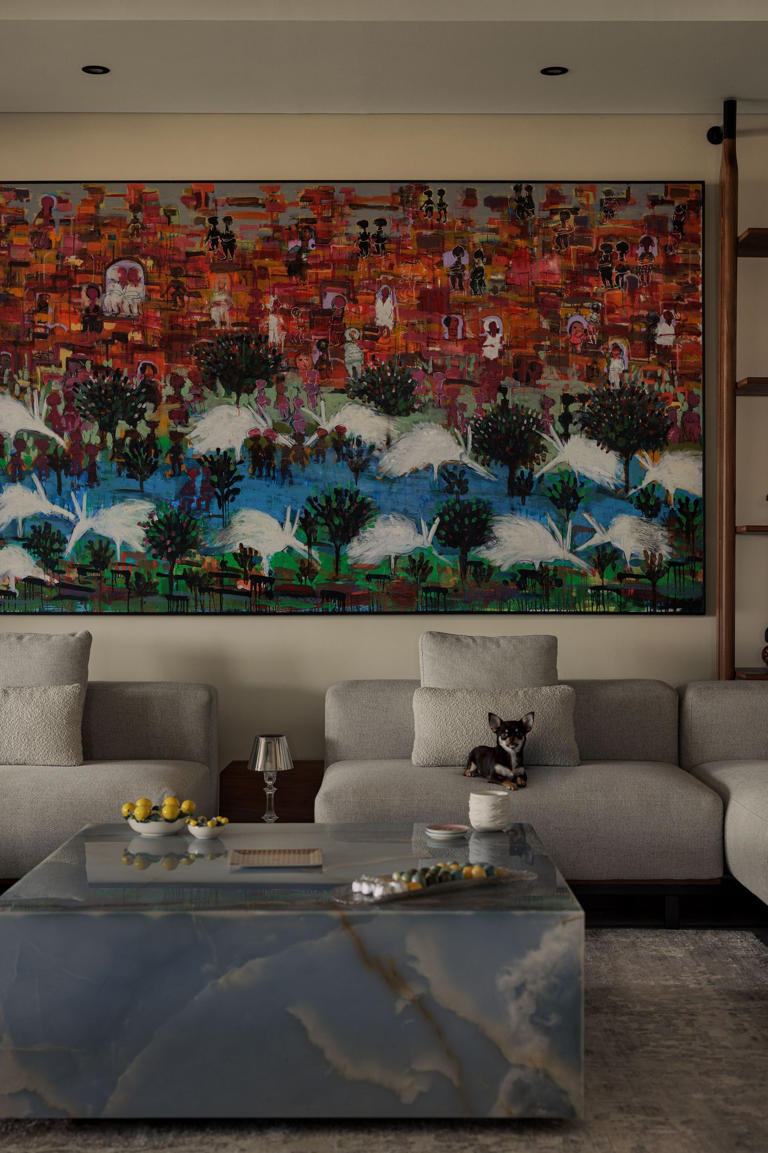 Elegant living room featuring large colorful painting above gray sectional sofa with blue marble coffee table.