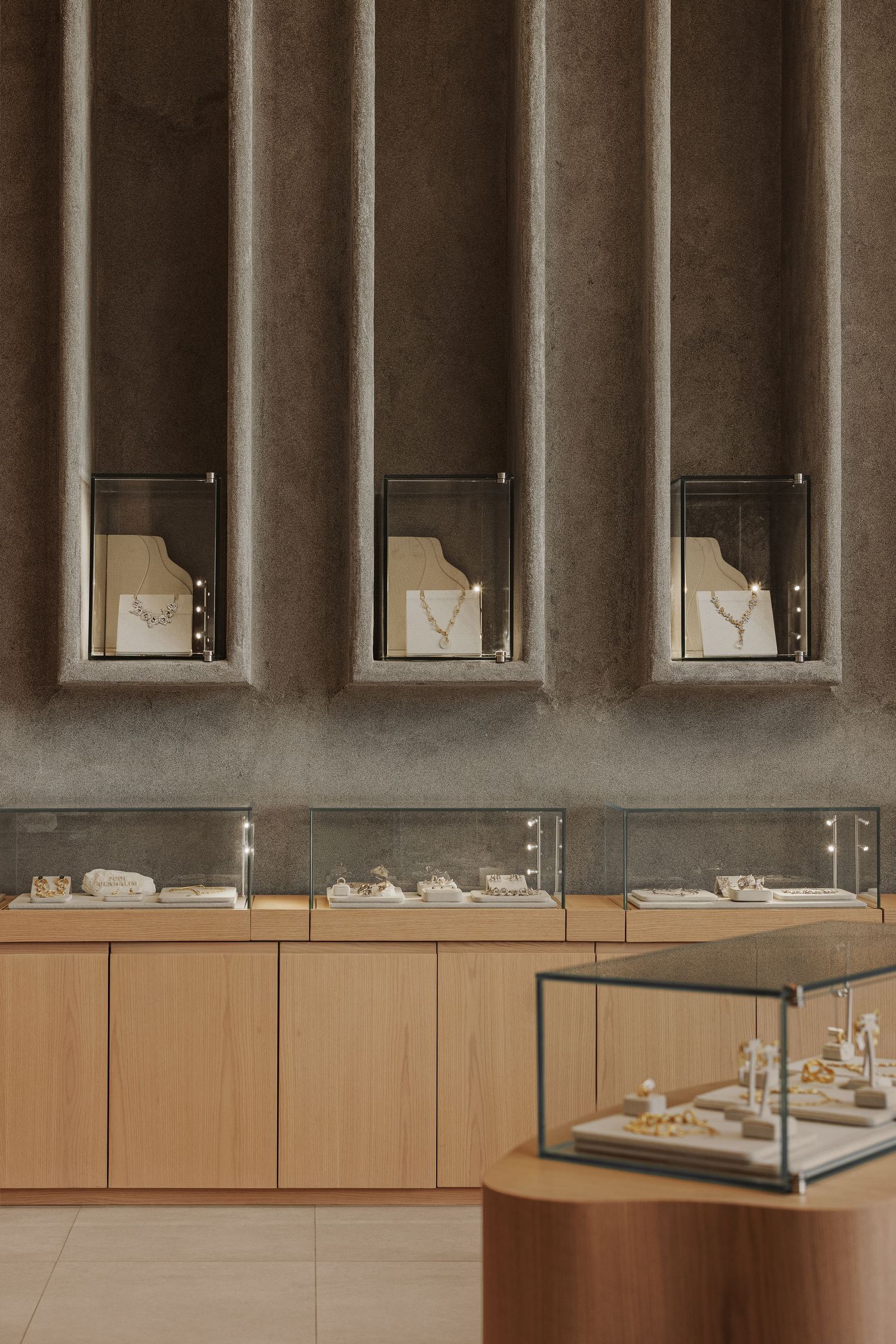 Luxury jewelry store interior with wooden display cases, glass showcases, and illuminated wall niches featuring gold necklaces.