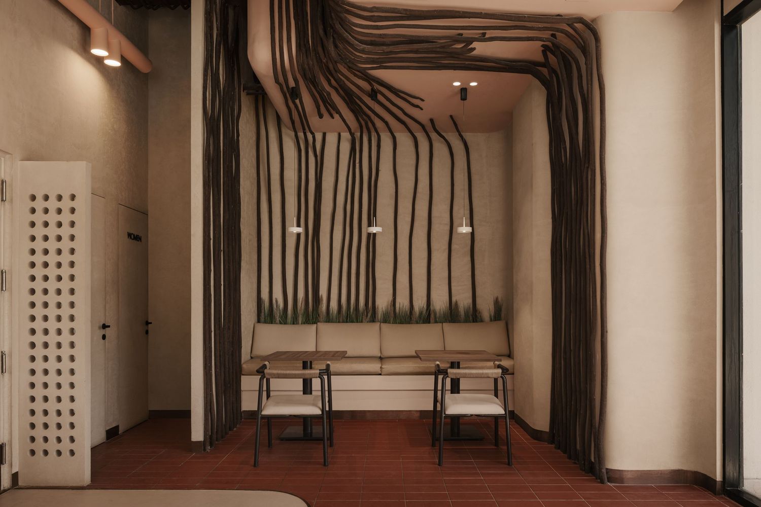 Rustic cafe interior with dark branch installations framing a cozy bench seating area with wooden chairs.