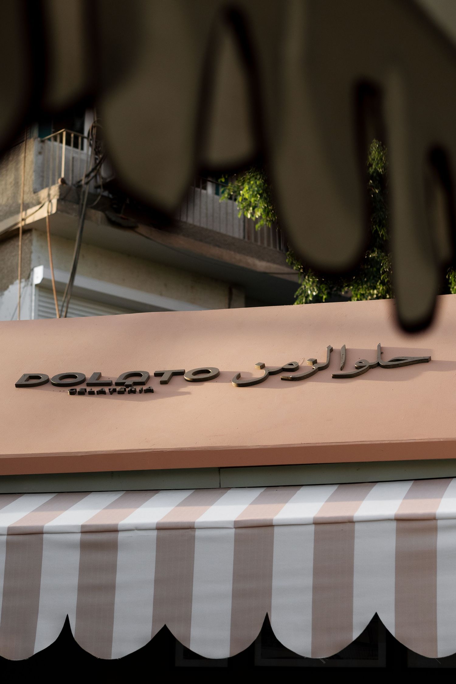 Dolato Gelateria shop sign with Arabic text and striped pink awning on a city street.