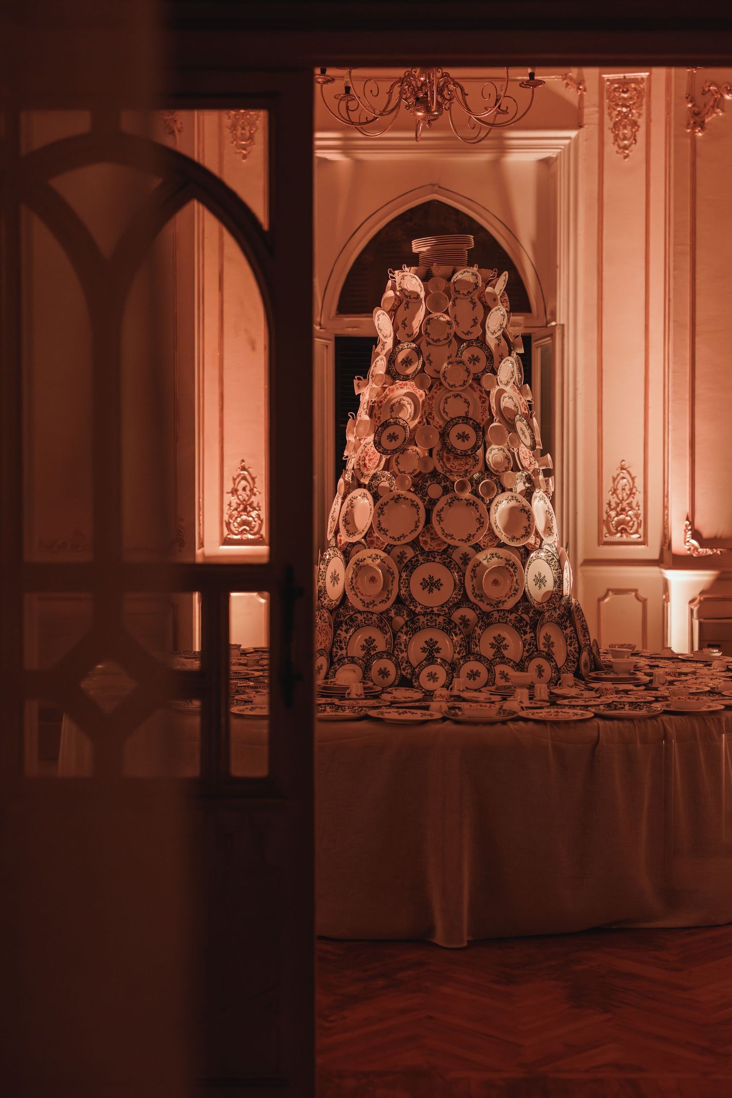 Dramatic view of a tall china plate tower display in an ornate room seen through an arched doorway.