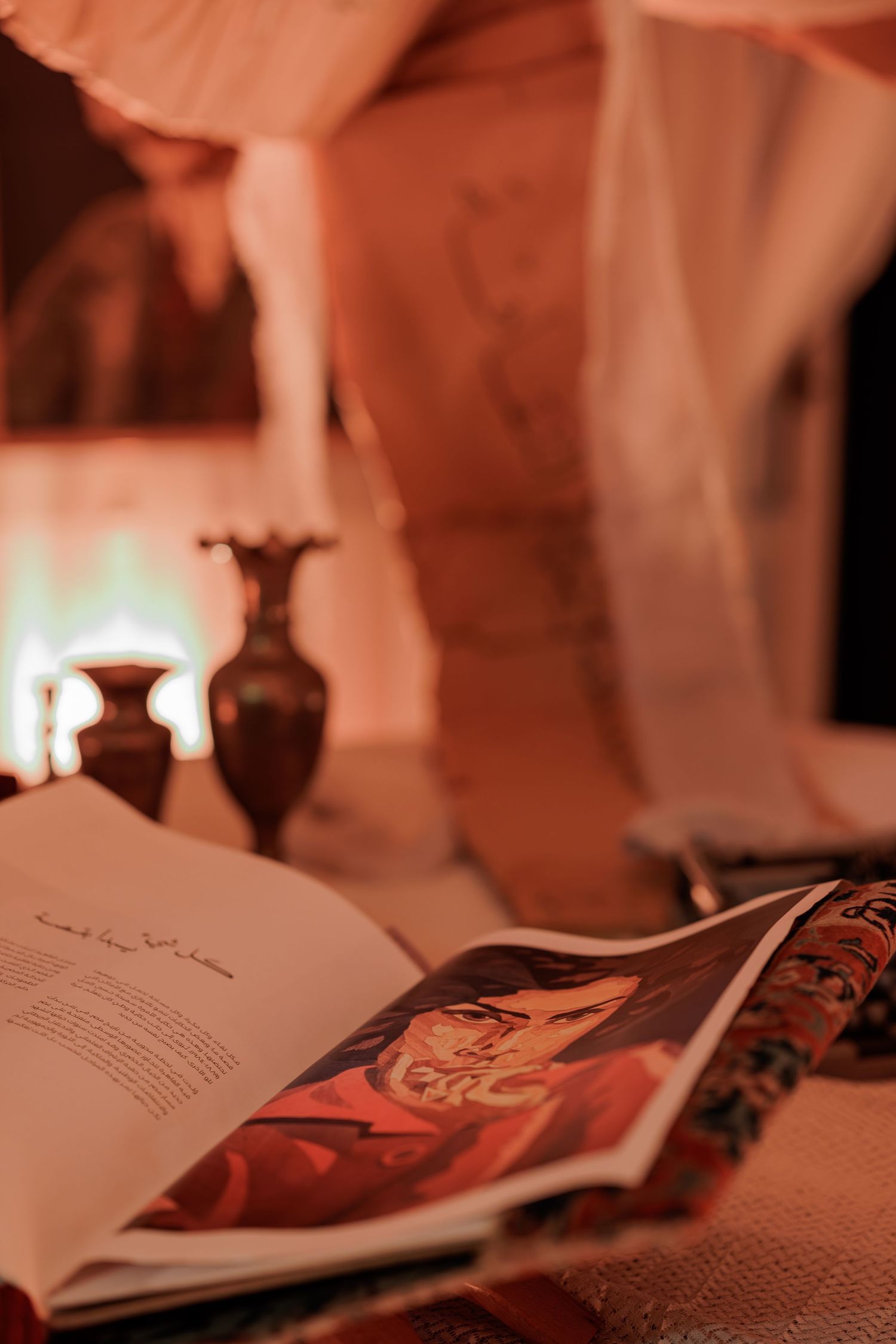 Open book with Arabic text and portrait illustration on a table with candles and vases in warm ambient light.