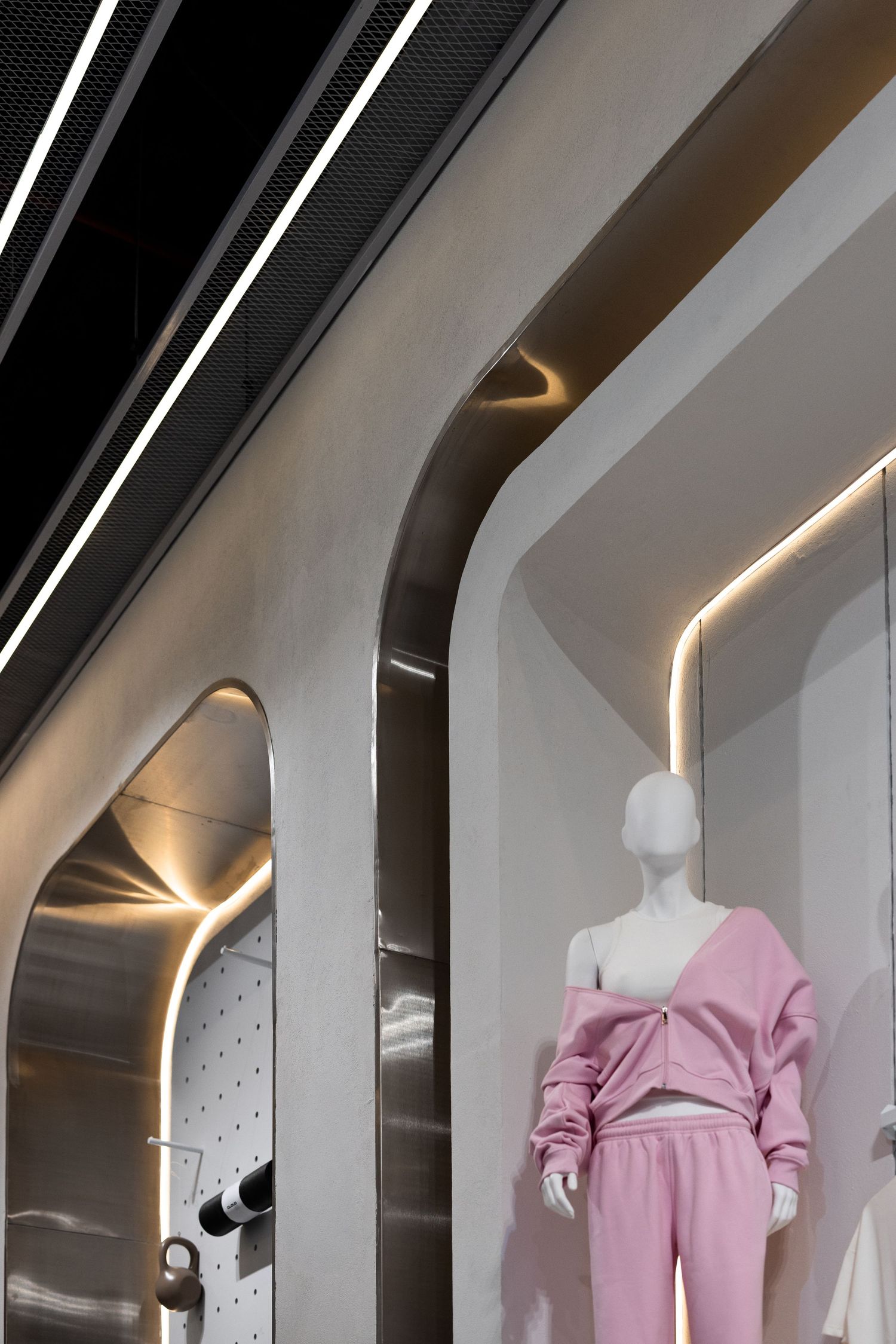 Futuristic boutique interior with curved silver walls, warm LED strip lighting, and mannequin dressed in pink tracksuit.