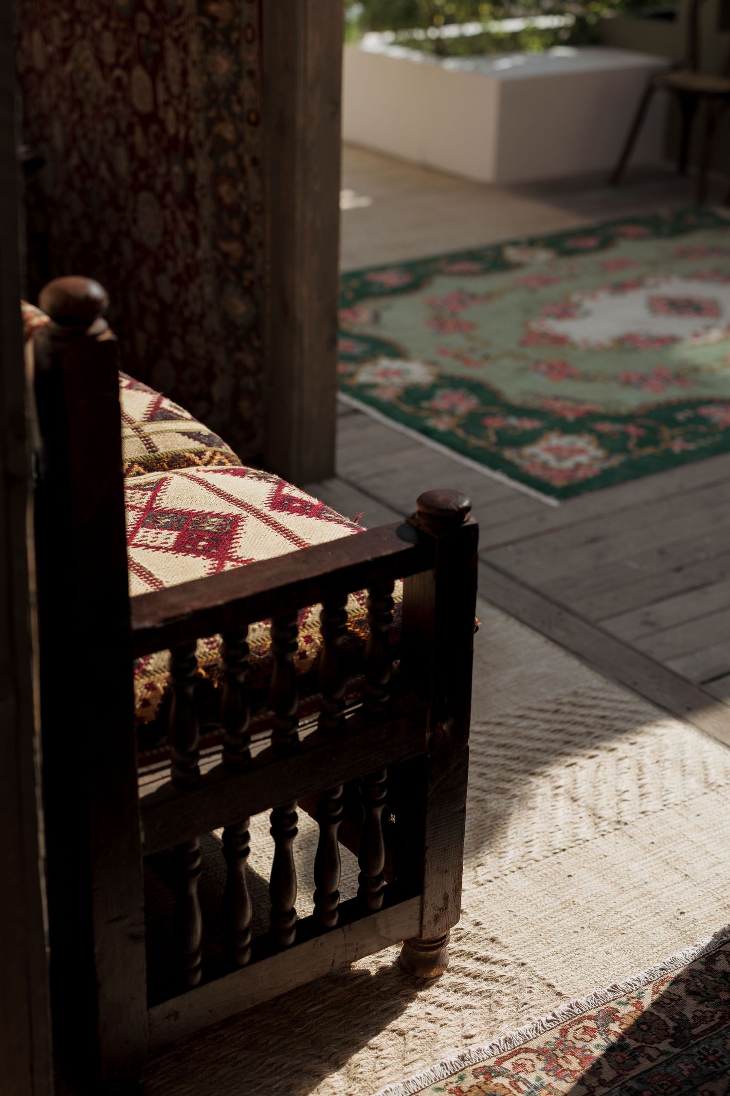 Antique dark wood chair with geometric cushion casting shadows on layered Persian rugs in sunlit interior space.