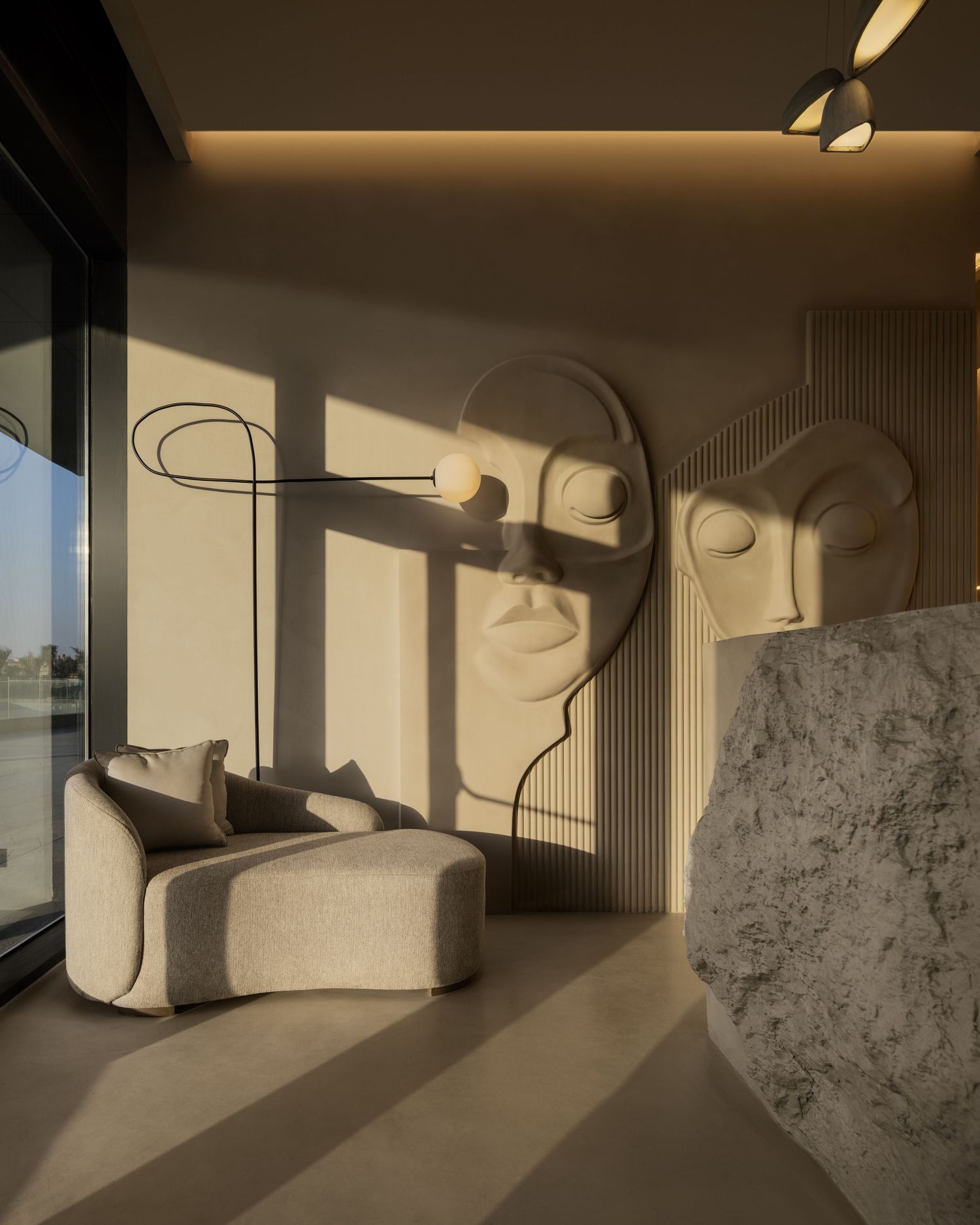 Modern interior with large beige sculptural face wall art, curved armchair, stone element, and warm ambient lighting.