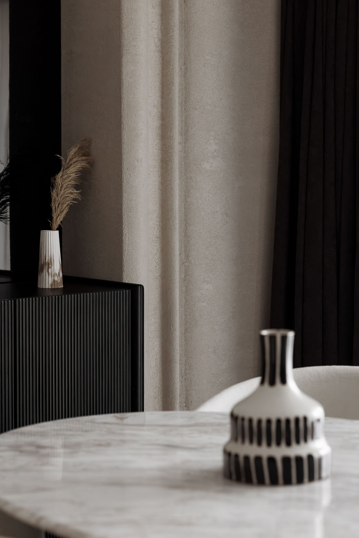Striped black and white ceramic vase on marble dining table with ribbed black sideboard in background.