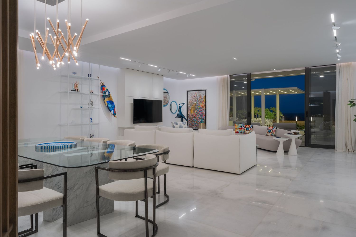 Spacious modern interior with glass dining table, white sofa, colorful artwork, and floor-to-ceiling windows.