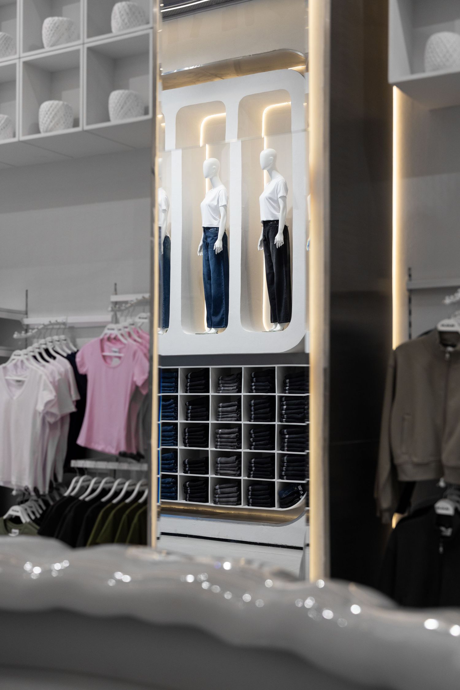 Fashion retail store interior showing mannequins in blue jeans displayed in illuminated white alcoves with folded clothing below.