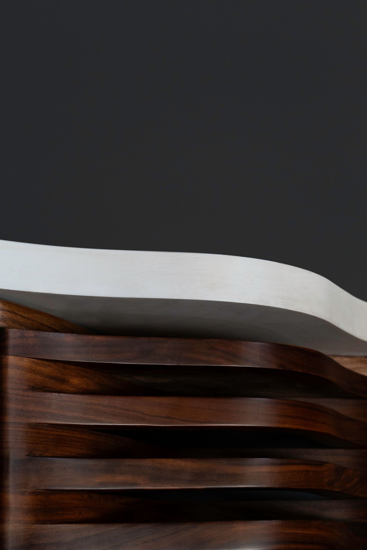 Minimalist close-up of curved white marble surface resting atop dark walnut wood slats.