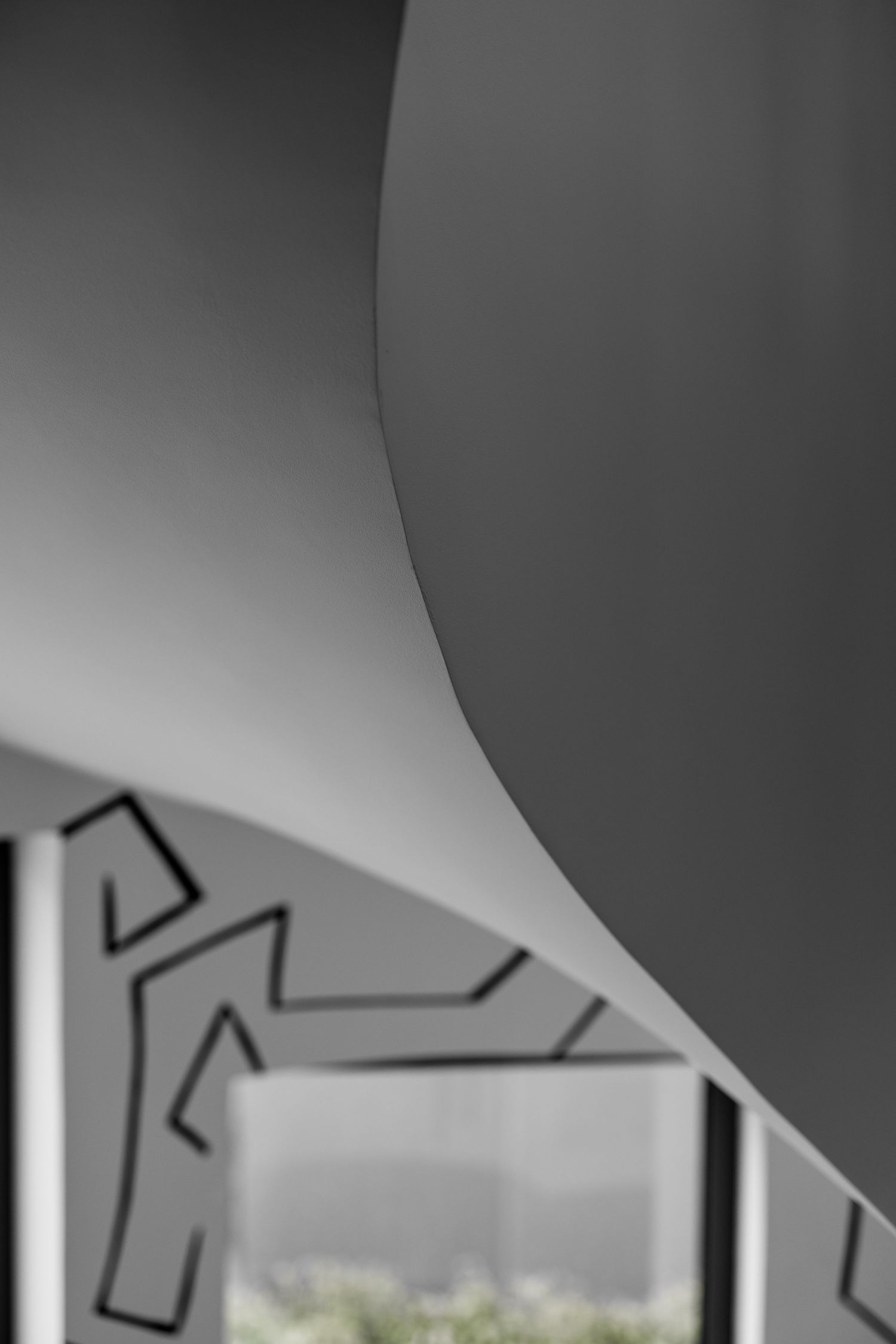 Abstract architectural detail of curved gray wall with blurred geometric black line art below.