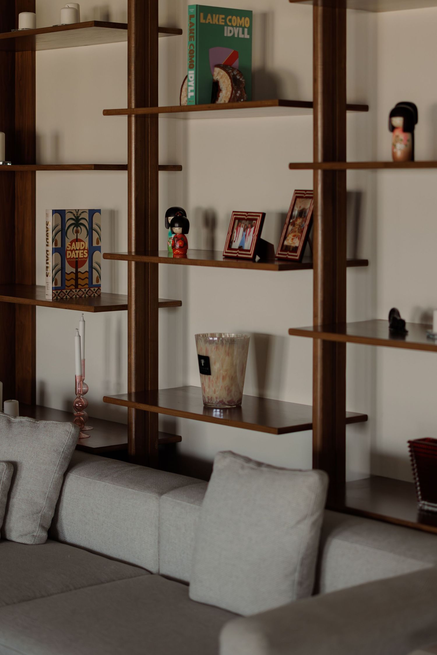 Wooden bookshelf displaying decorative items including kokeshi dolls, framed photos, books, and glass vase.