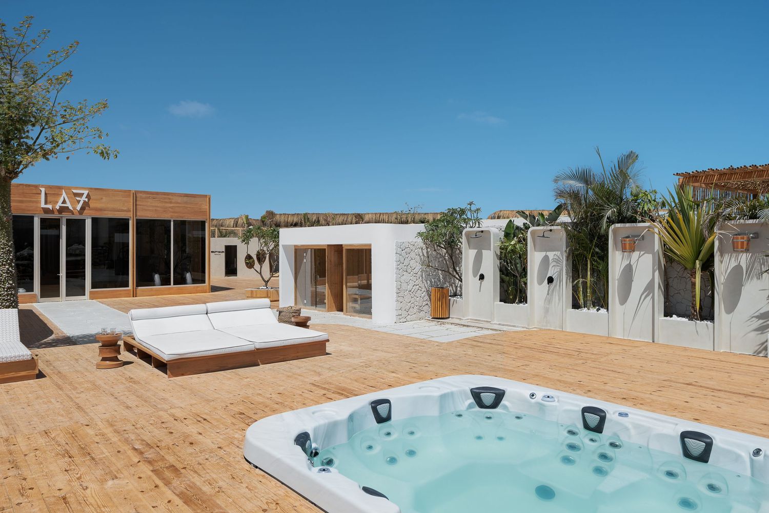 Rooftop terrace at LA7 featuring a white jacuzzi, sun loungers, outdoor showers, and lush tropical landscaping.