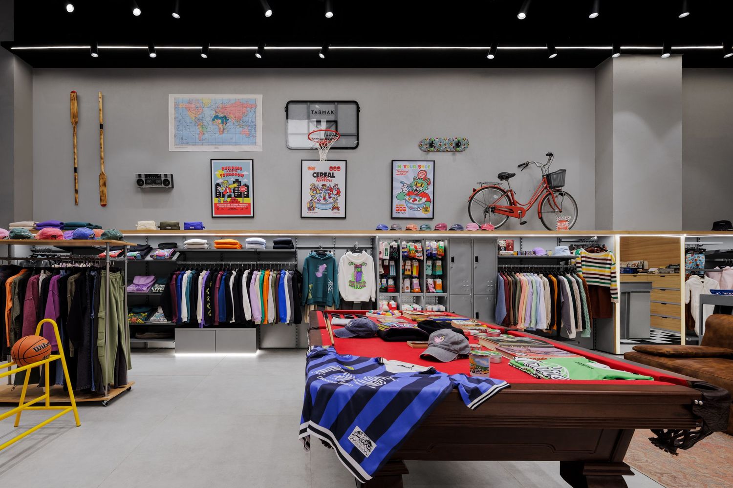 Trendy streetwear retail store interior with pool table display, clothing racks, posters, and a red bicycle mounted on the wall.