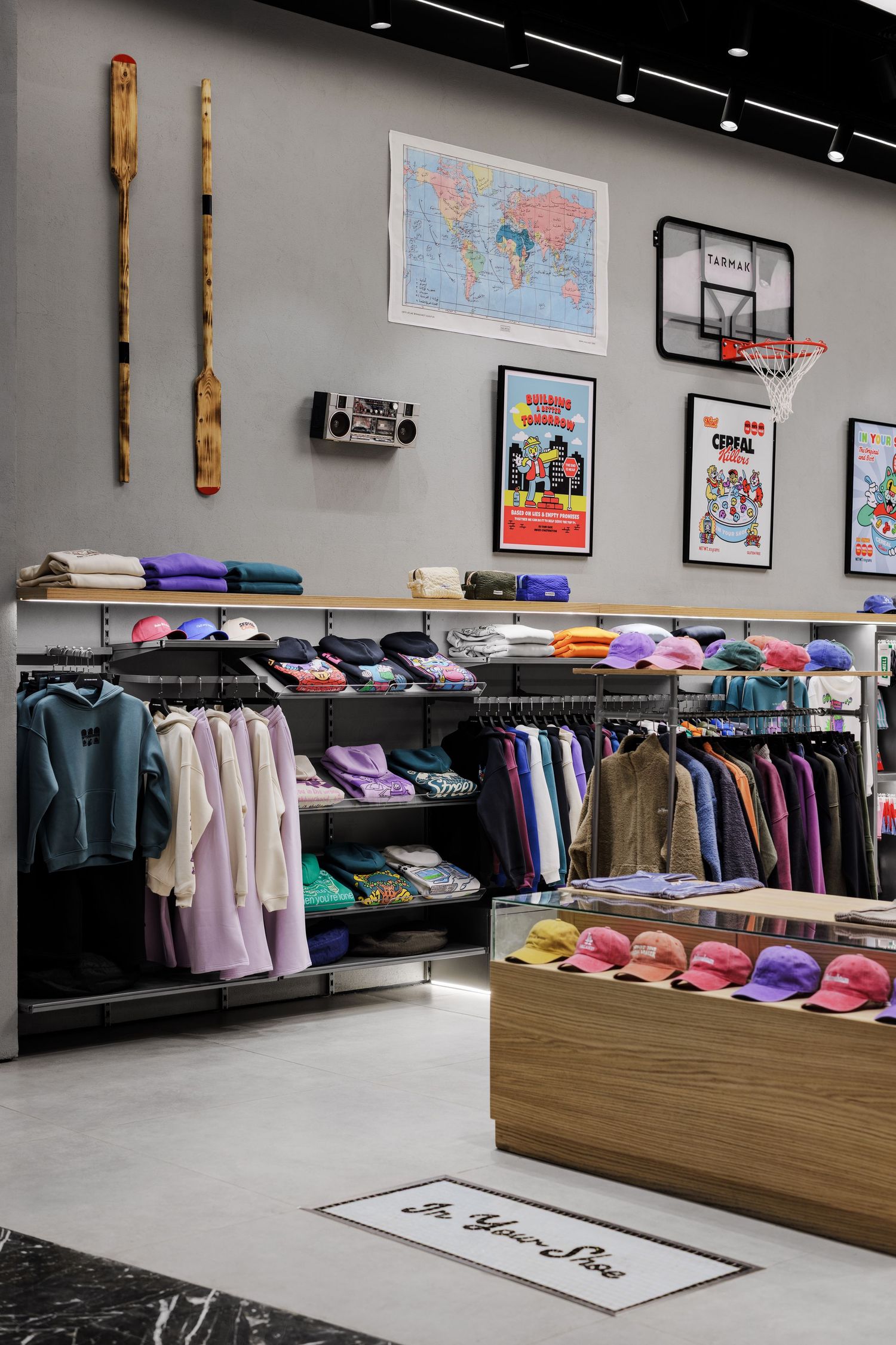 Colorful streetwear clothing store with rainbow caps, hanging apparel, shelves, and eclectic wall decor including a world map.