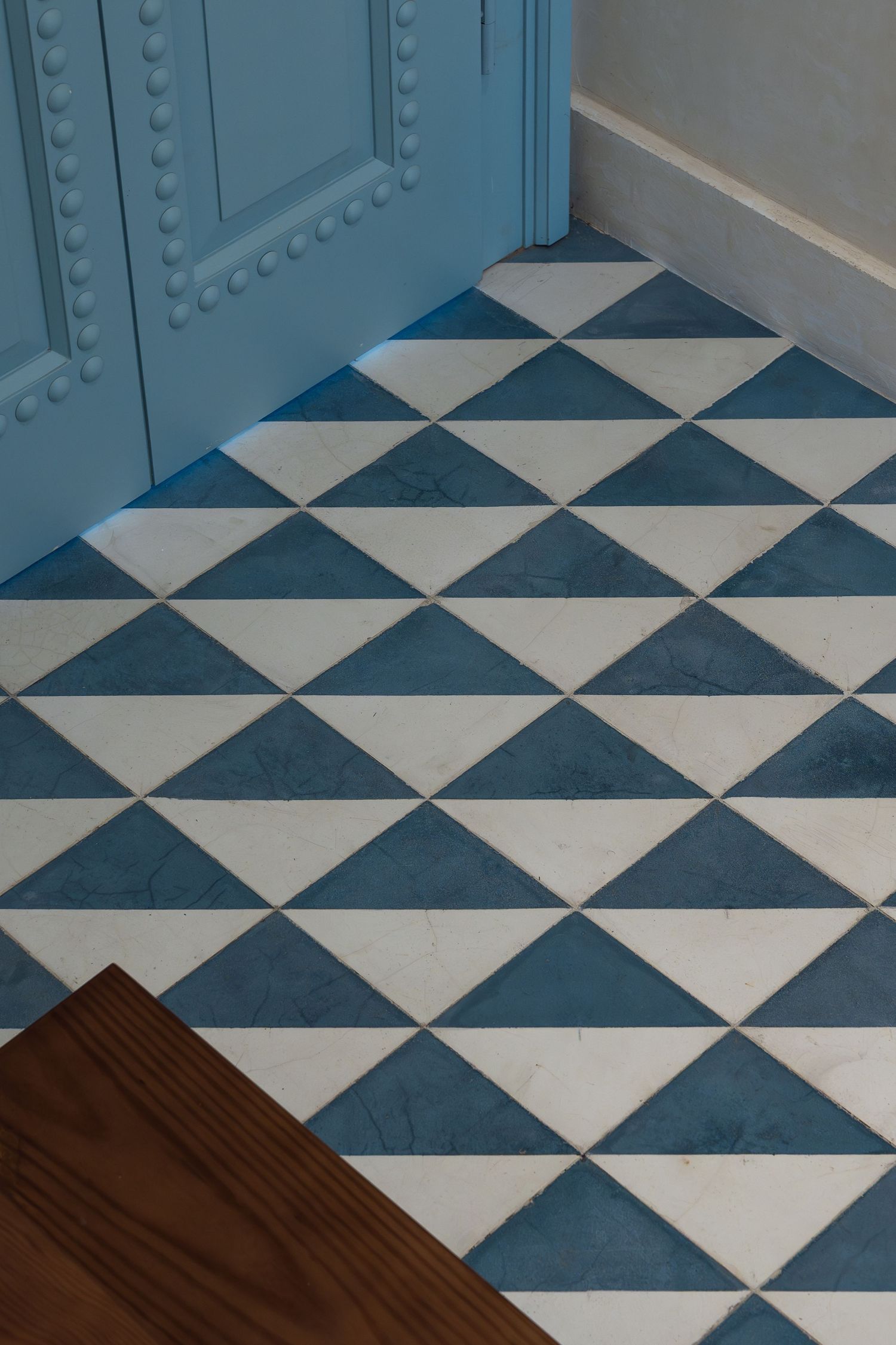 Blue and white geometric triangle pattern floor tiles next to an ornate blue painted door.