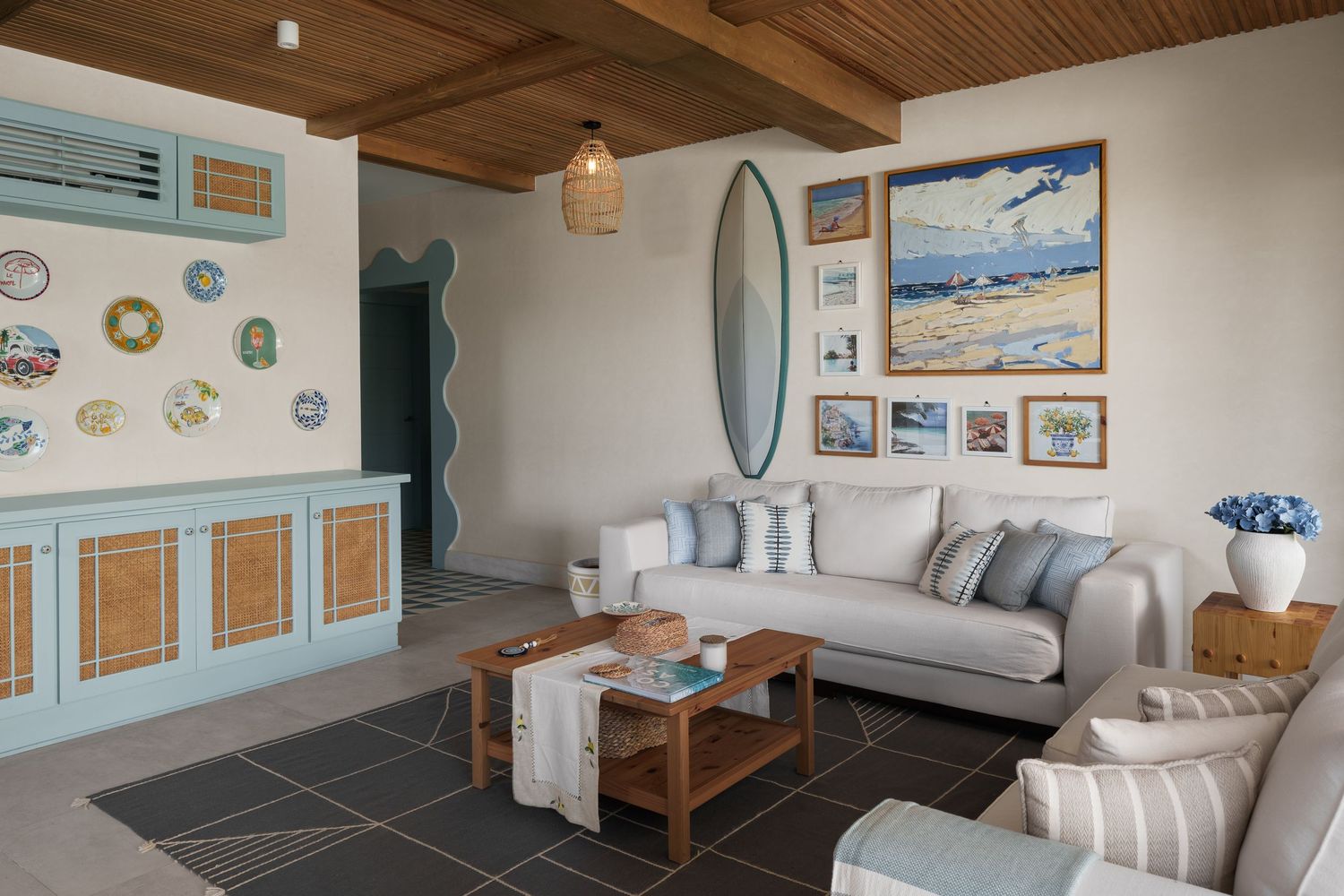Coastal living room featuring surfboard, blue cabinetry, rattan accents, and beach-inspired artwork.