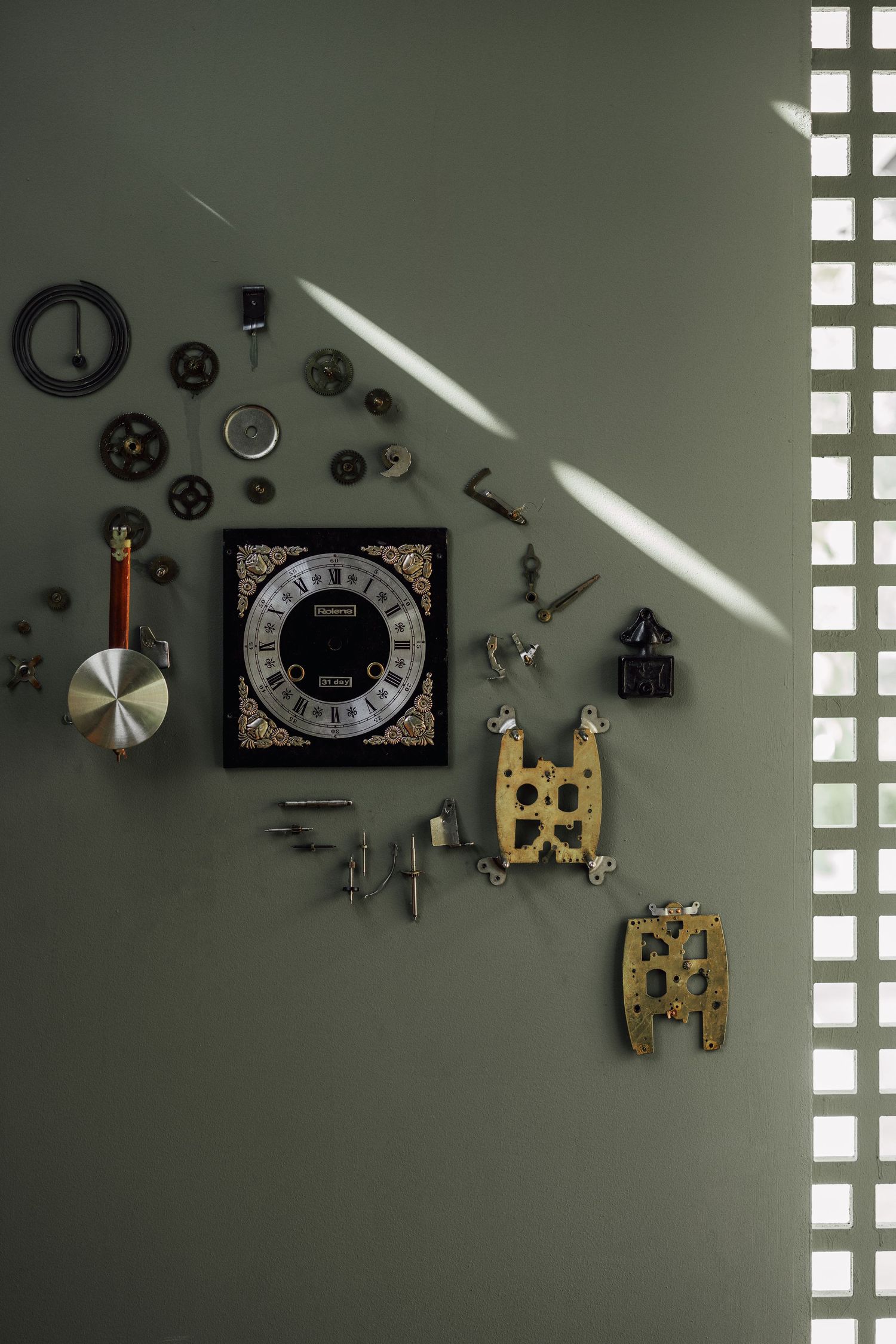 Vintage clock parts and gears arranged as wall art on a sage green wall with natural light.