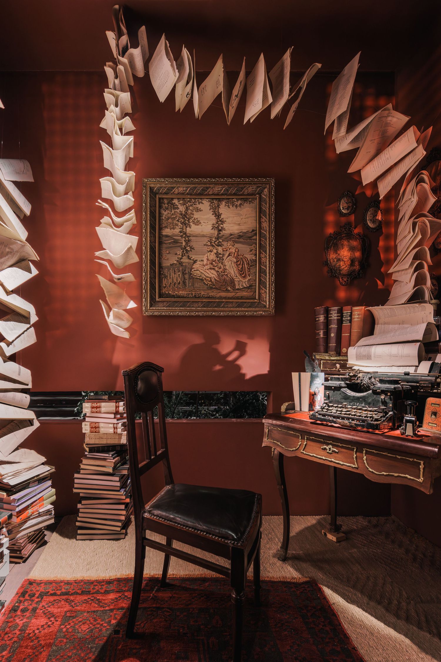 Surreal room installation featuring suspended open books, stacked novels, and a vintage typewriter.