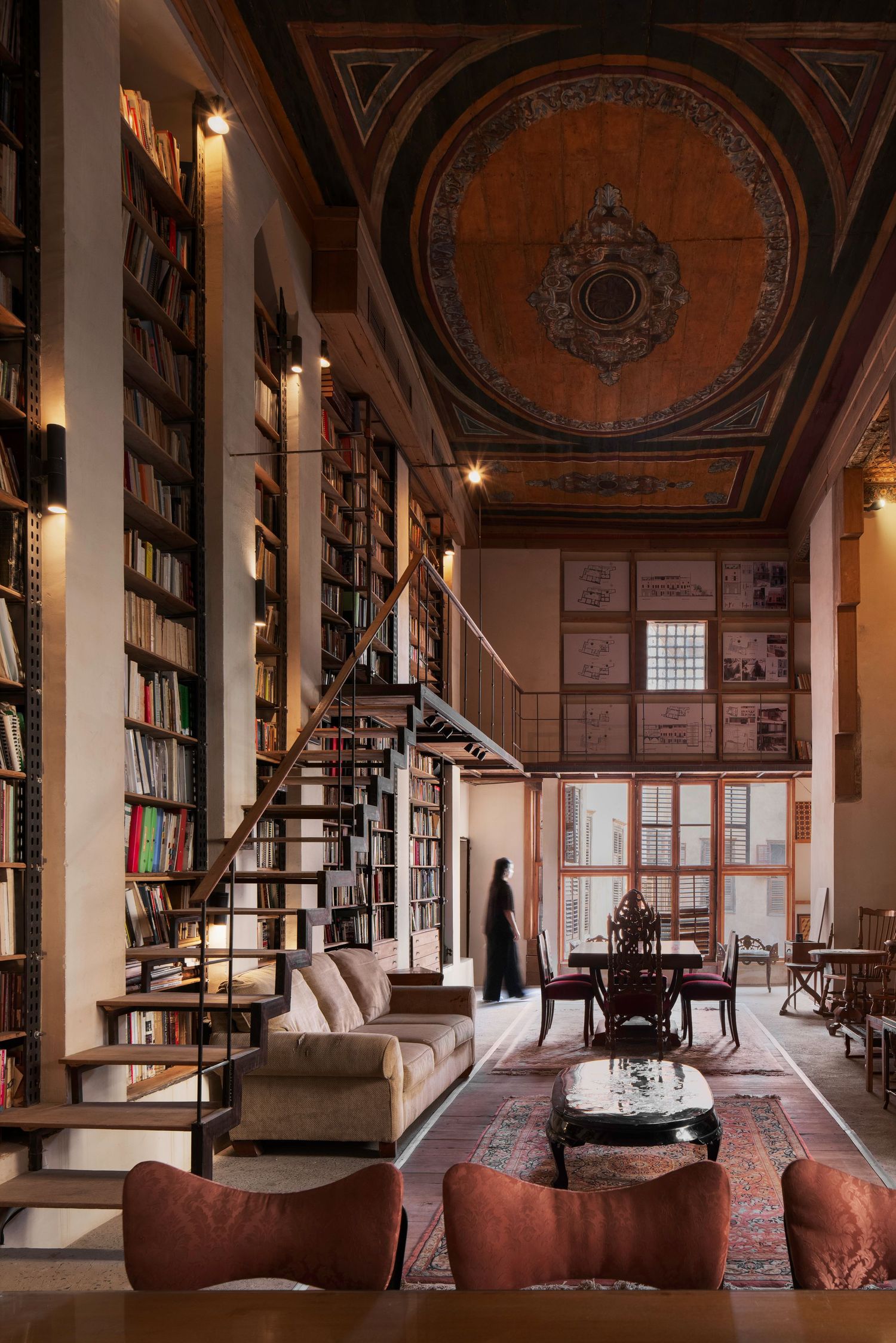 Grand two-story library with floor-to-ceiling bookshelves, ornate painted ceiling dome, Persian rug, and elegant seating.