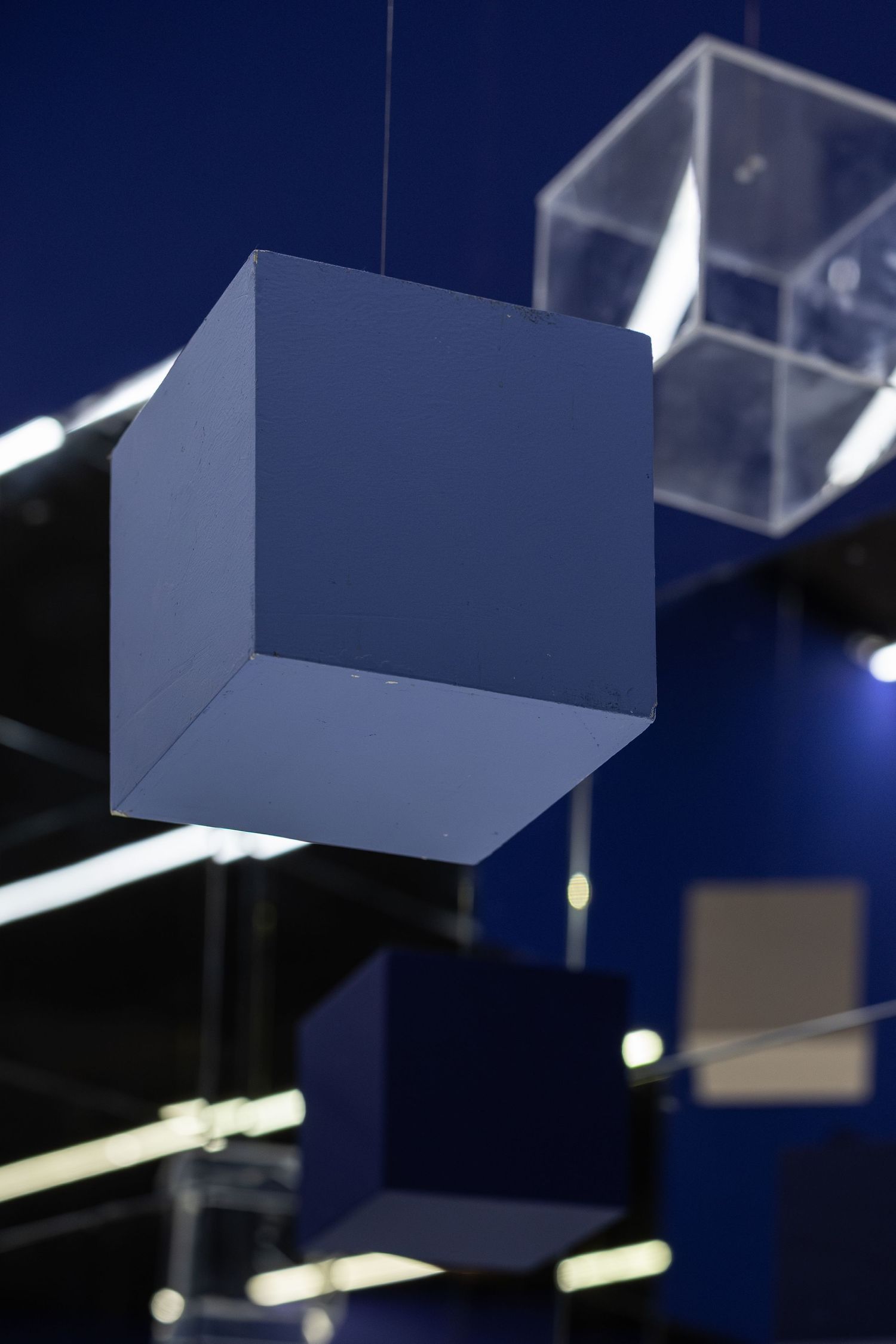 Blue and transparent acrylic cubes suspended from the ceiling against a dark blue background.