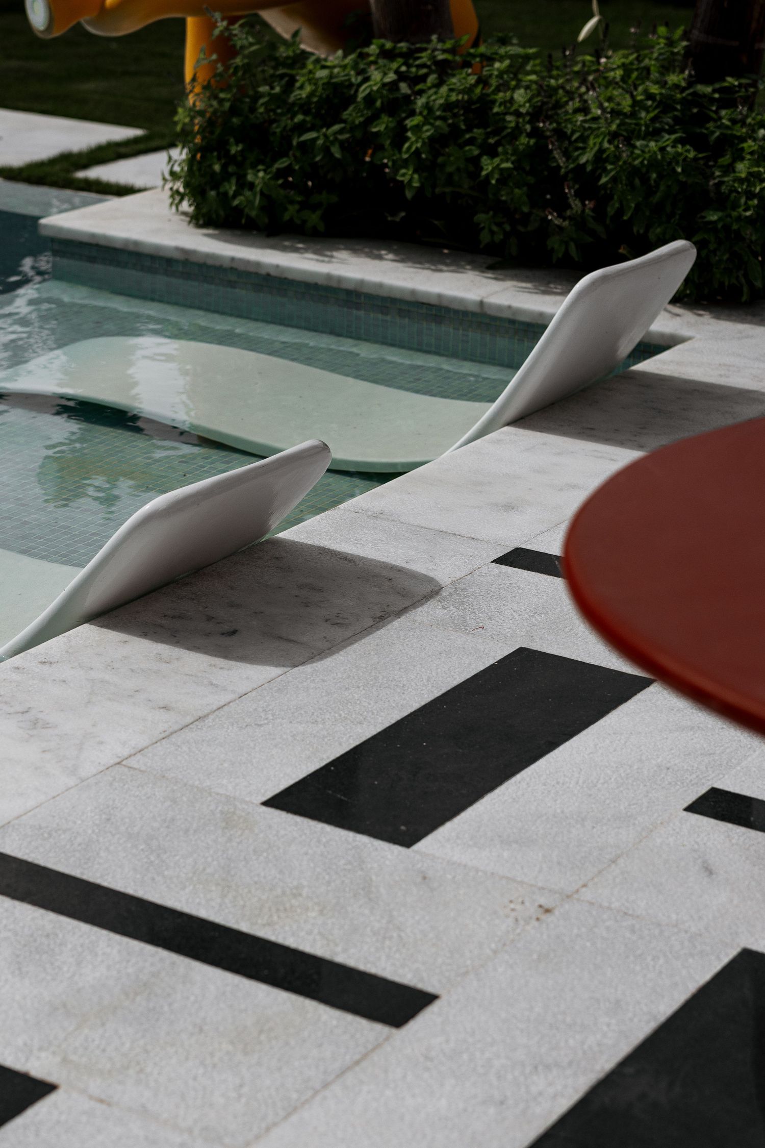 White sculptural pool loungers on bold geometric black and white marble tiles beside turquoise pool.