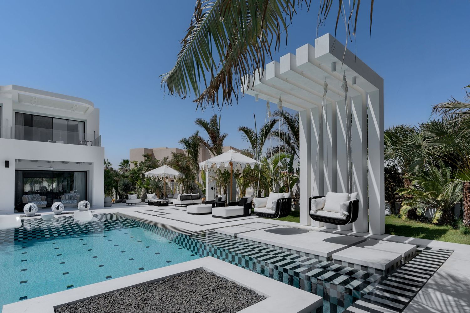 Stunning luxury villa with geometric white pergola, black and white tiled pool, and tropical palm trees.