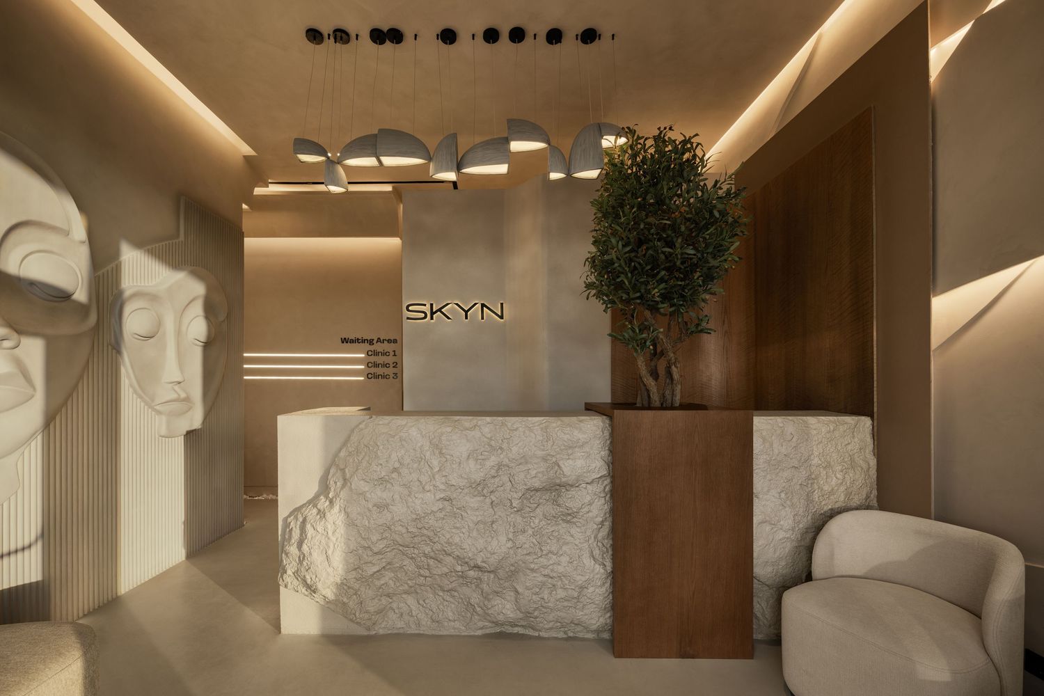 Elegant SKYN clinic reception desk featuring white marble counter, warm wood accents, and decorative tree.