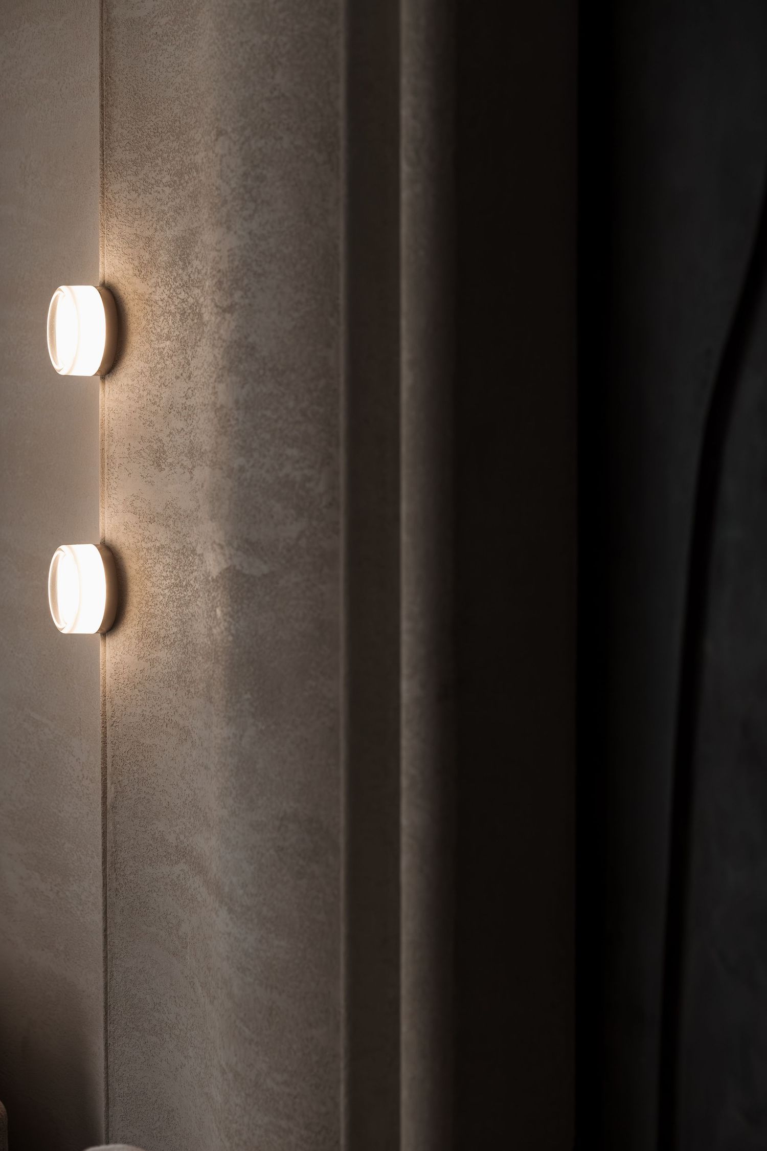 Two square wall-mounted lights glowing warmly on a textured gray concrete wall in a modern interior.