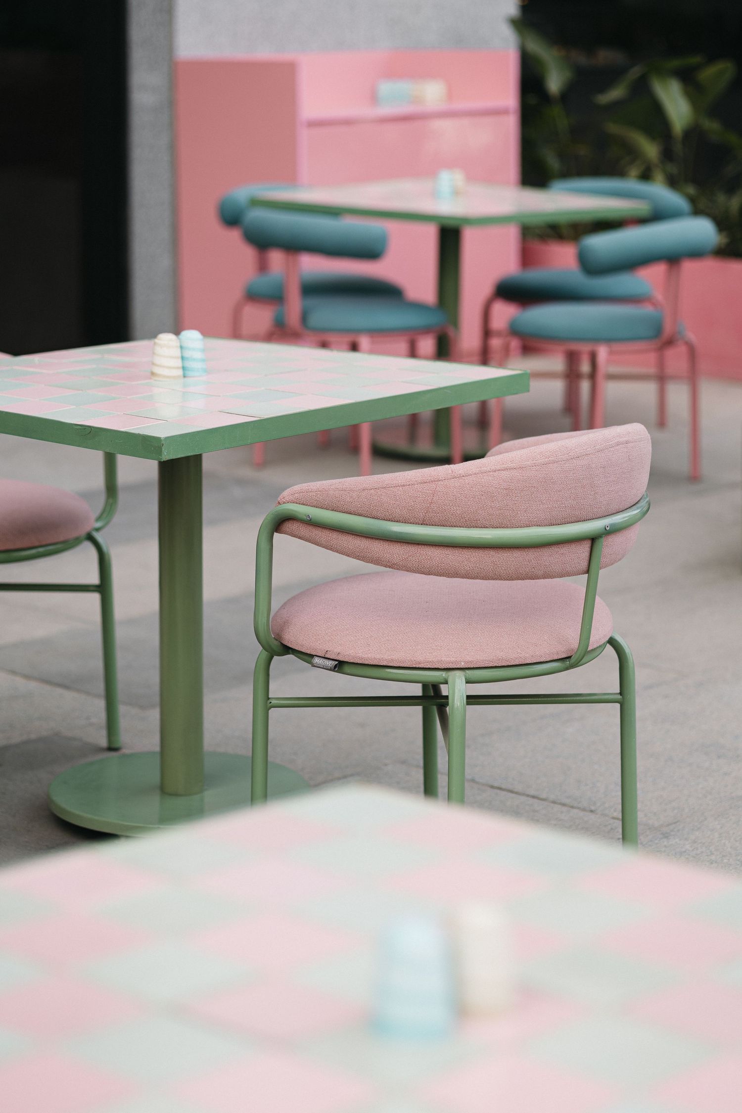 Close-up of pink cushioned chair and checkerboard green table at outdoor cafe.