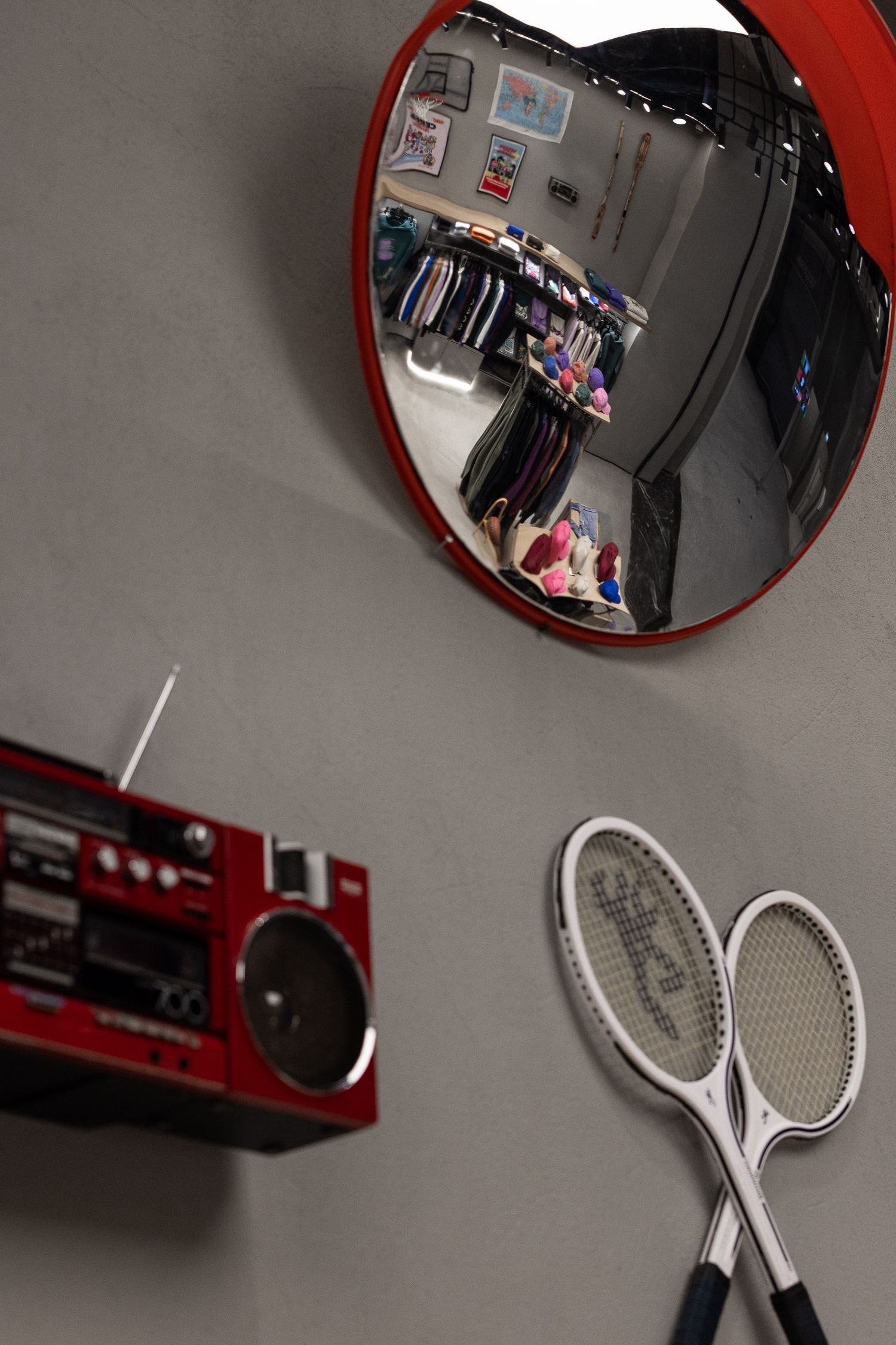 Wall-mounted convex mirror, red vintage boombox, and white tennis rackets decorating a retail store wall.