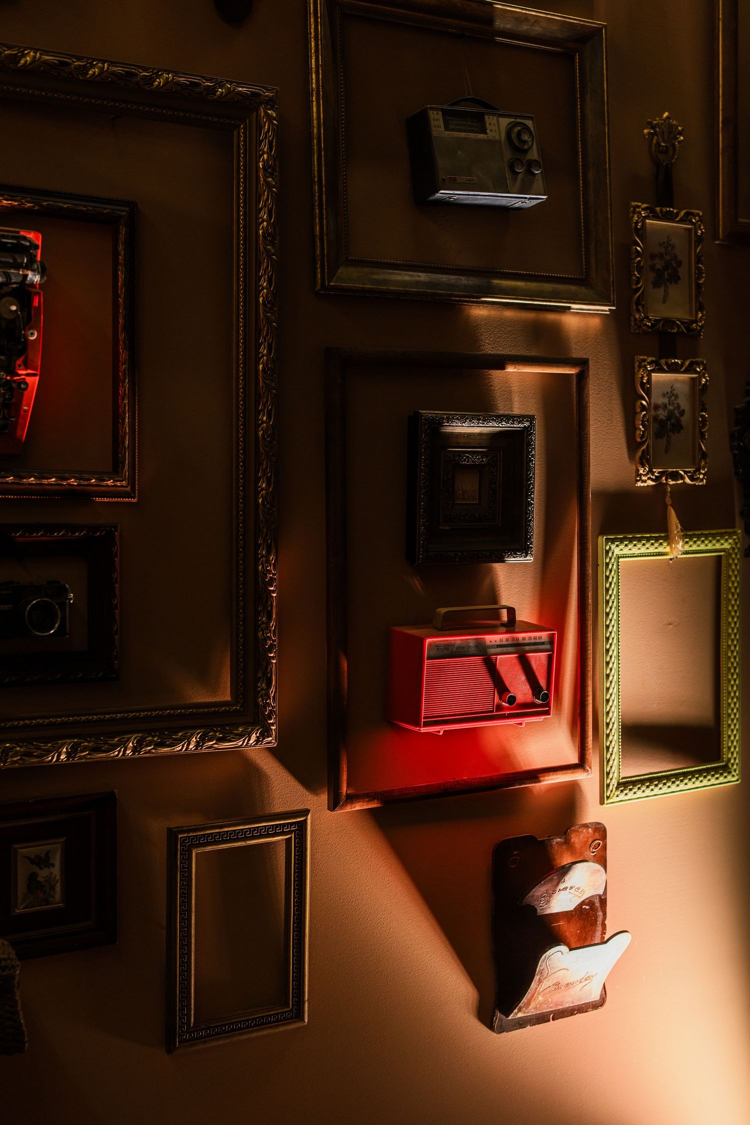 Collection of ornate gold picture frames on dark wall displaying vintage radios and antique cameras.