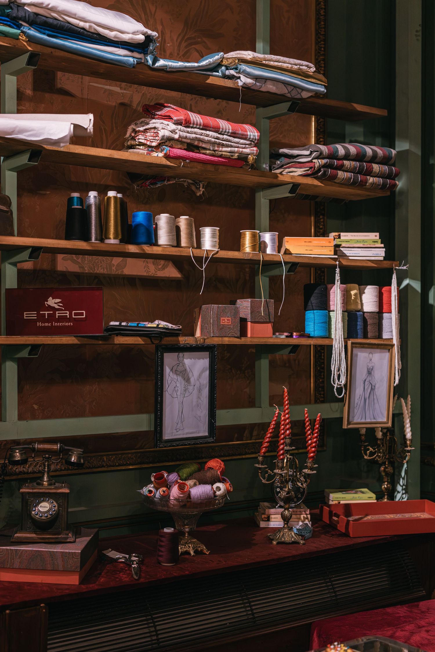 Elegant fashion atelier shelving with folded fabrics, thread spools, sketch frames, candelabra, and Etro branding.
