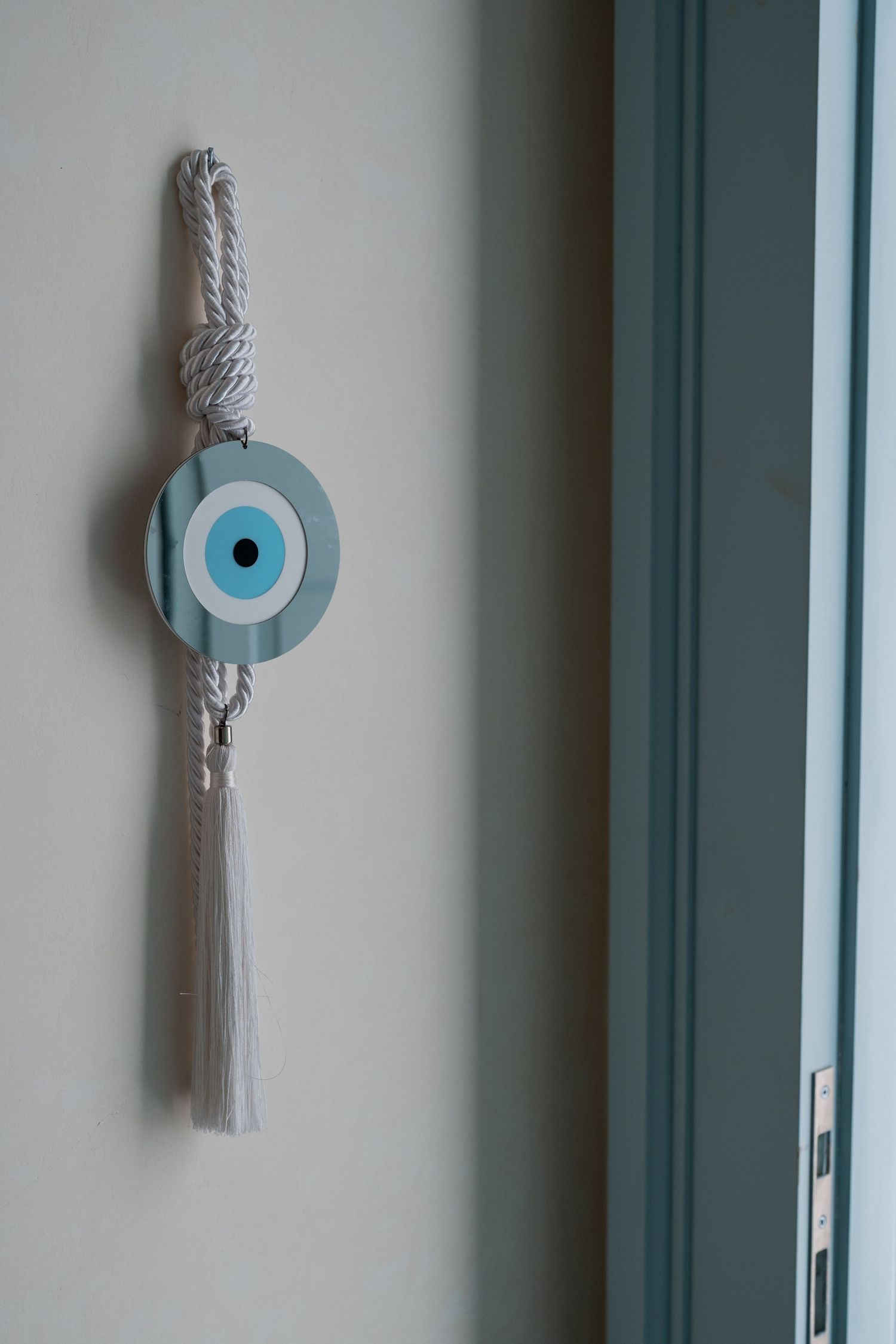 Traditional Turkish evil eye amulet hanging on a white wall beside a light blue door frame.