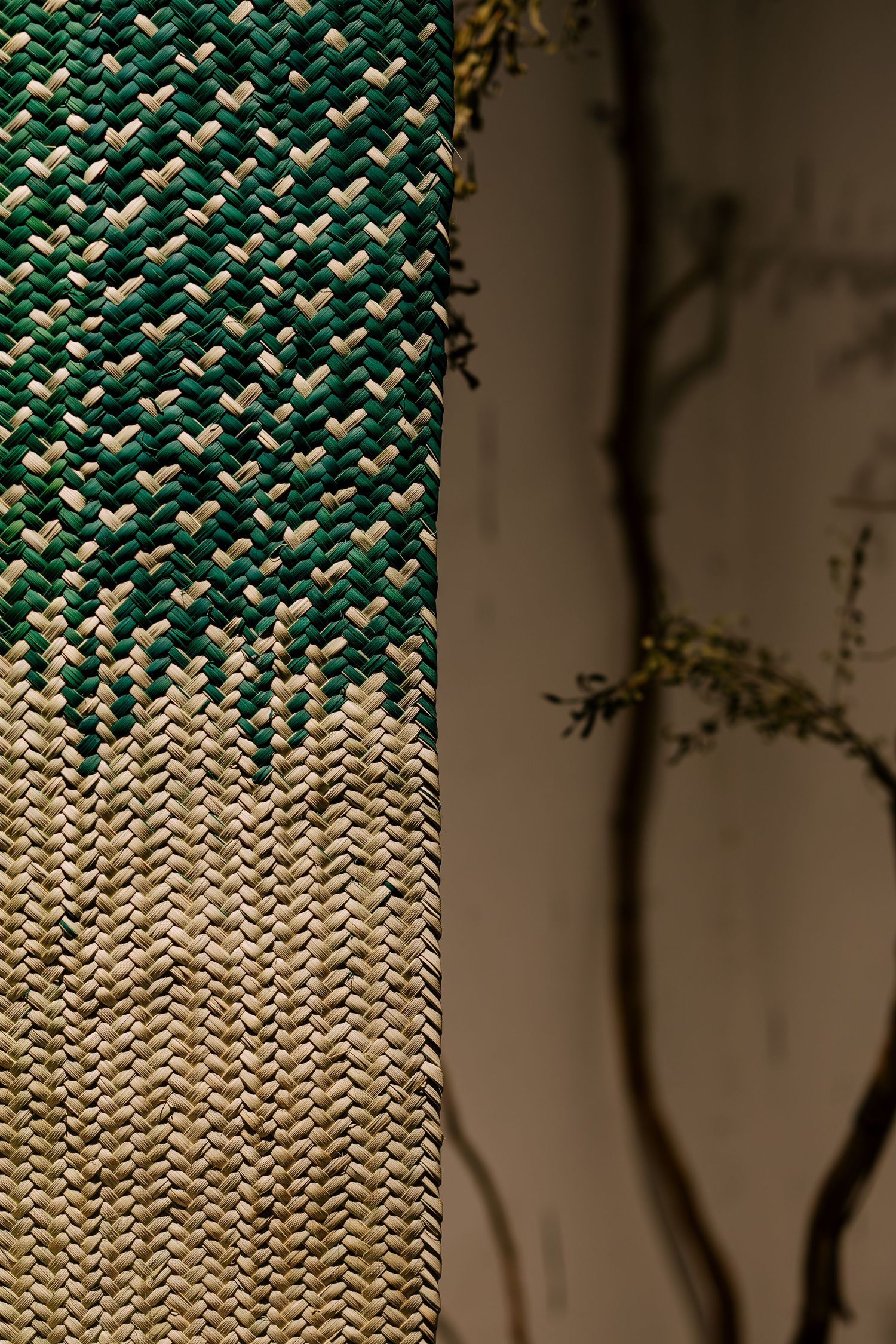 Close-up of green and natural woven textile panel with intricate herringbone pattern beside bare branches.
