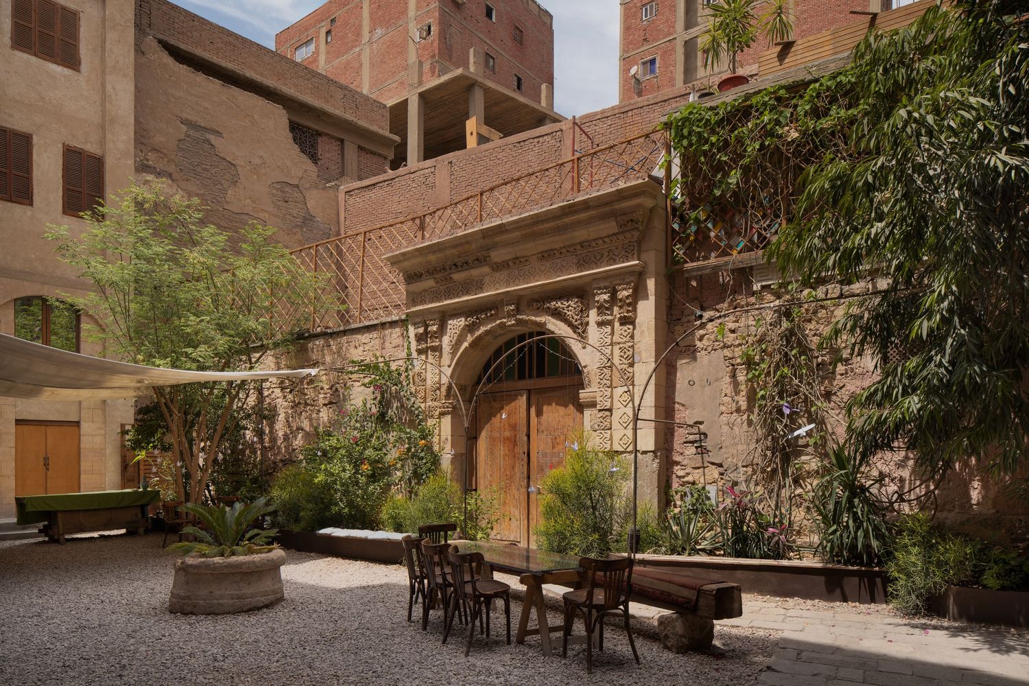 Historic stone courtyard with arched wooden door, lush greenery, and outdoor dining furniture in Cairo.