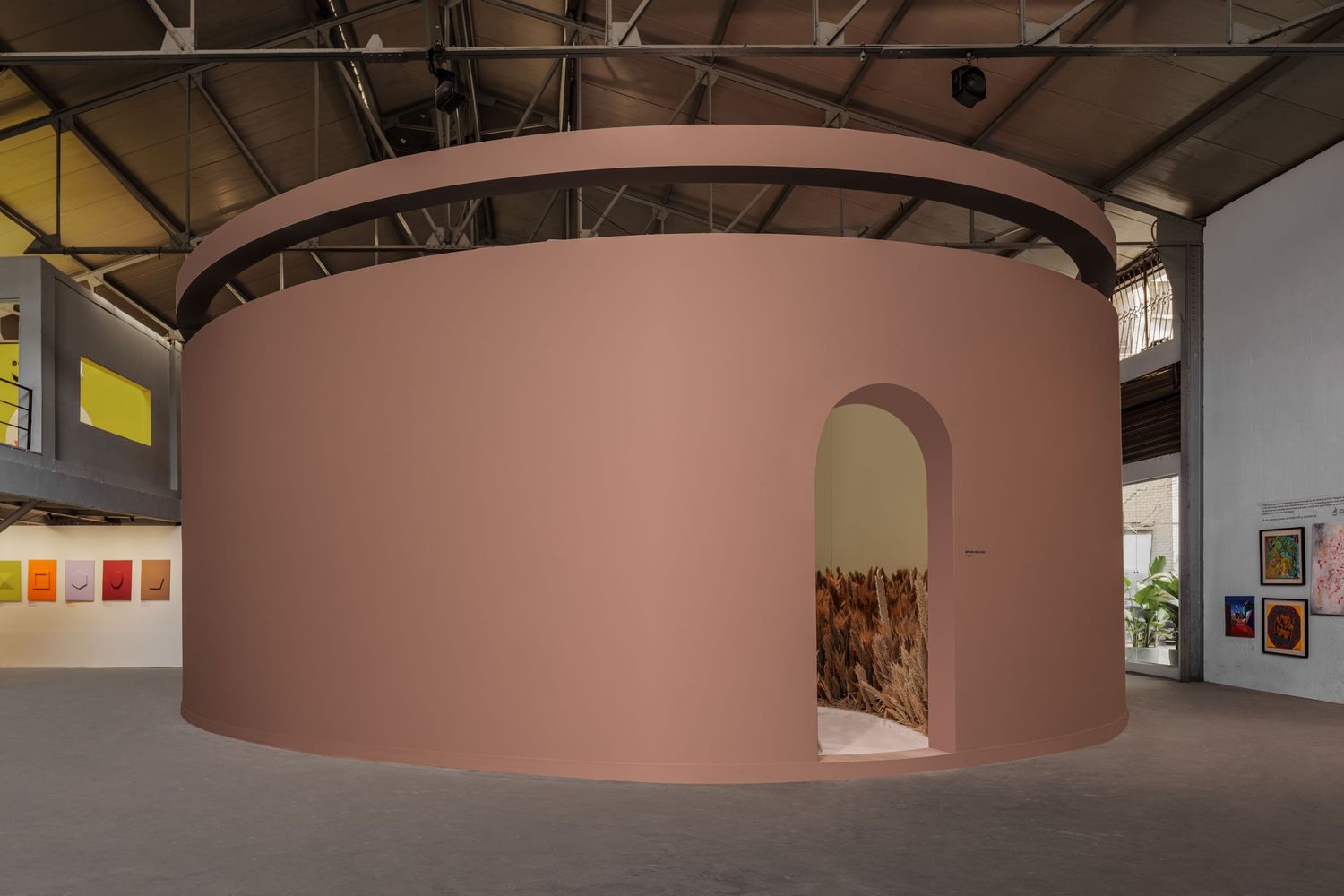 Pink circular cylindrical art installation with arched openings revealing textured interior in gallery space.