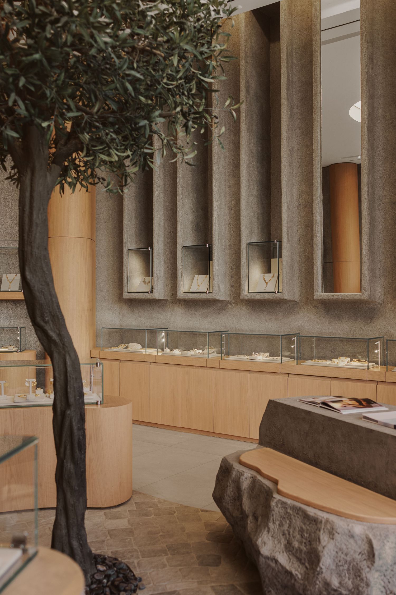 Elegant jewelry boutique interior featuring an olive tree, stone surfaces, and illuminated display cases.