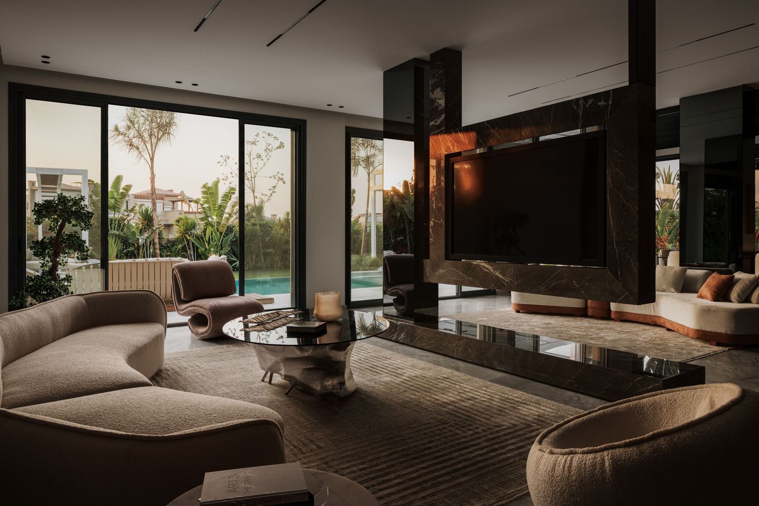 Contemporary living room with curved beige sofa, dark fireplace feature wall, large TV, and pool views.
