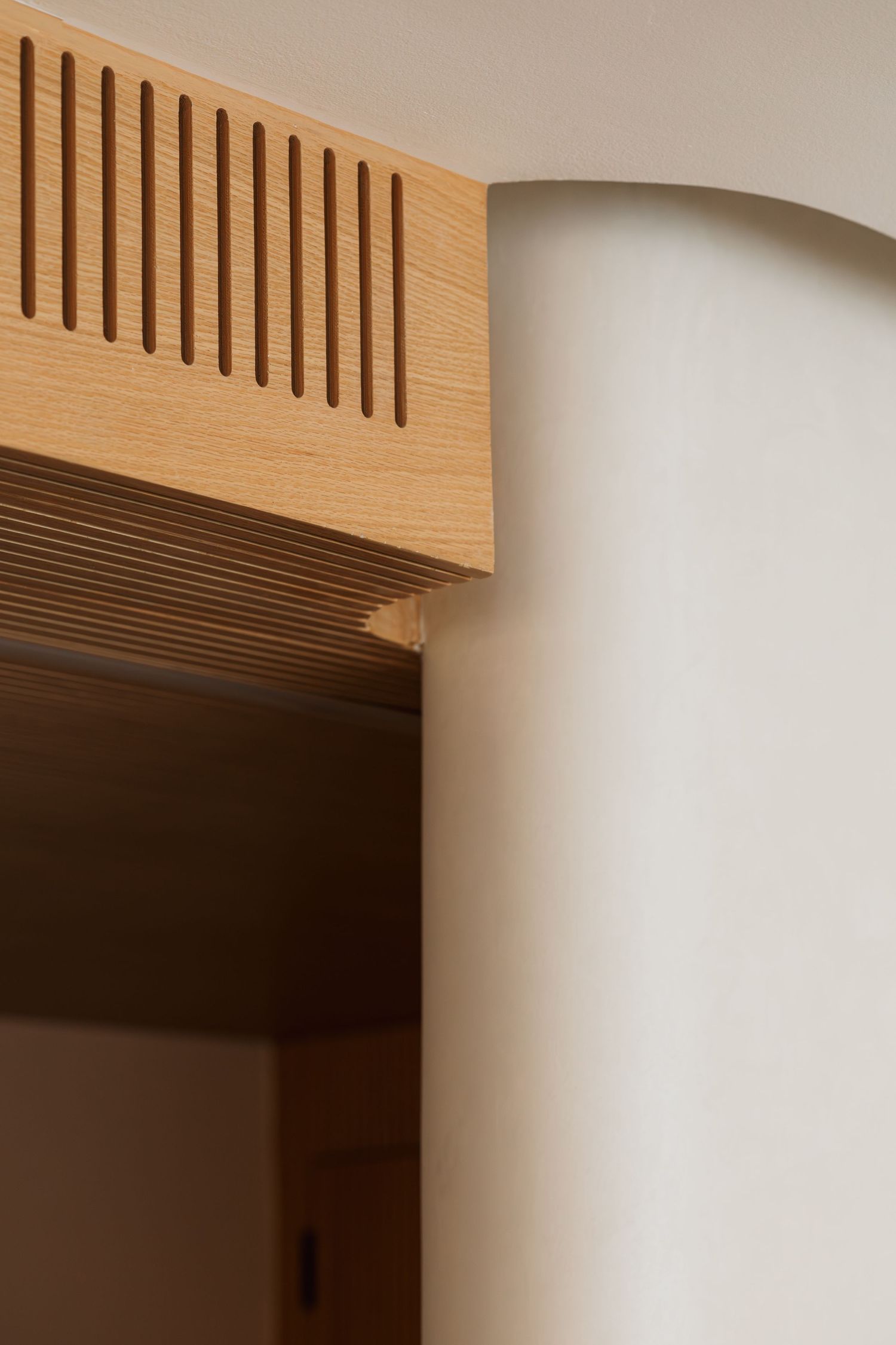 Close-up architectural detail of slatted oak wood ceiling beam meeting curved white plaster wall in modern interior.