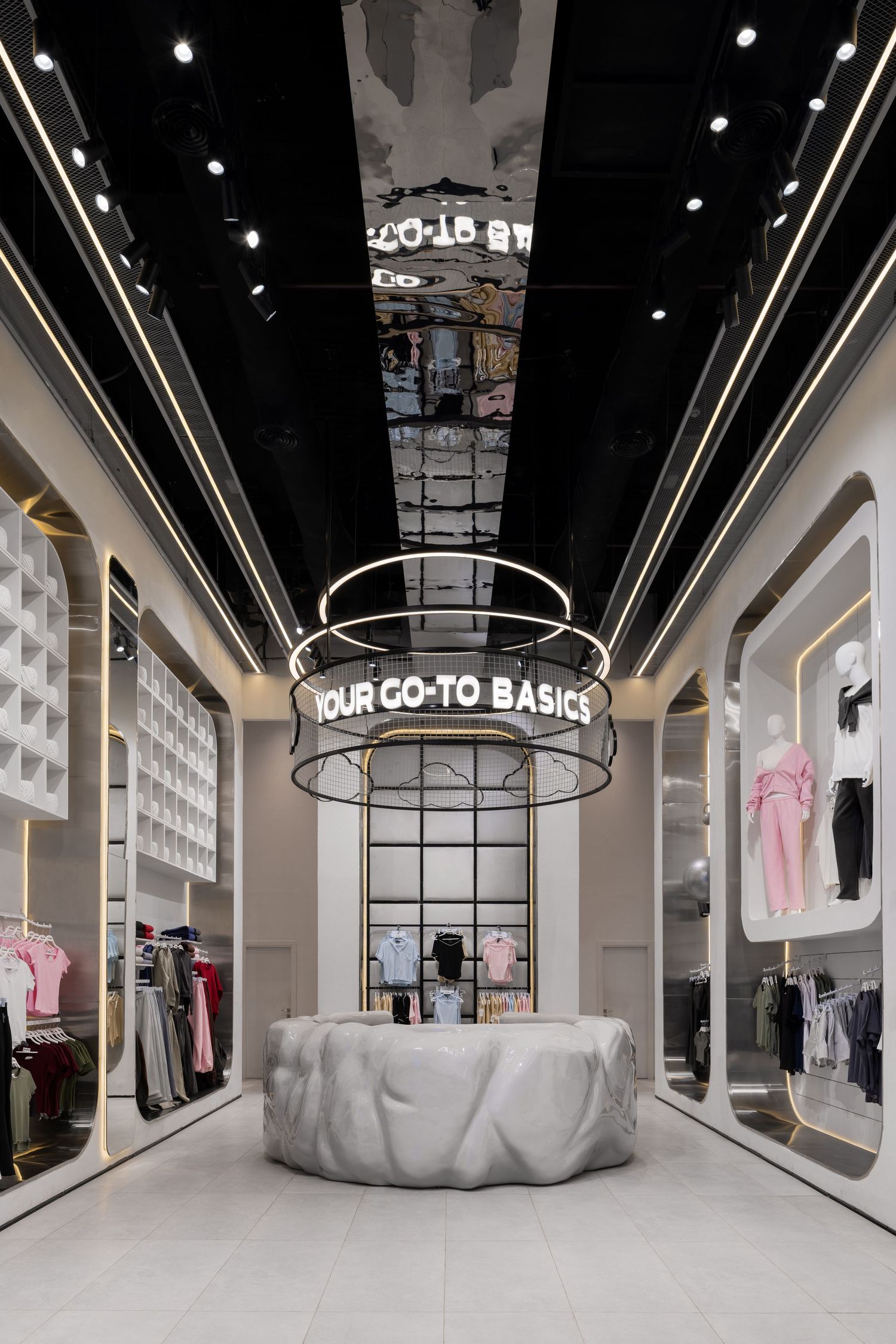 Modern retail store interior with circular display fixture and illuminated YOUR GO-TO BASICS sign above marble pedestal.