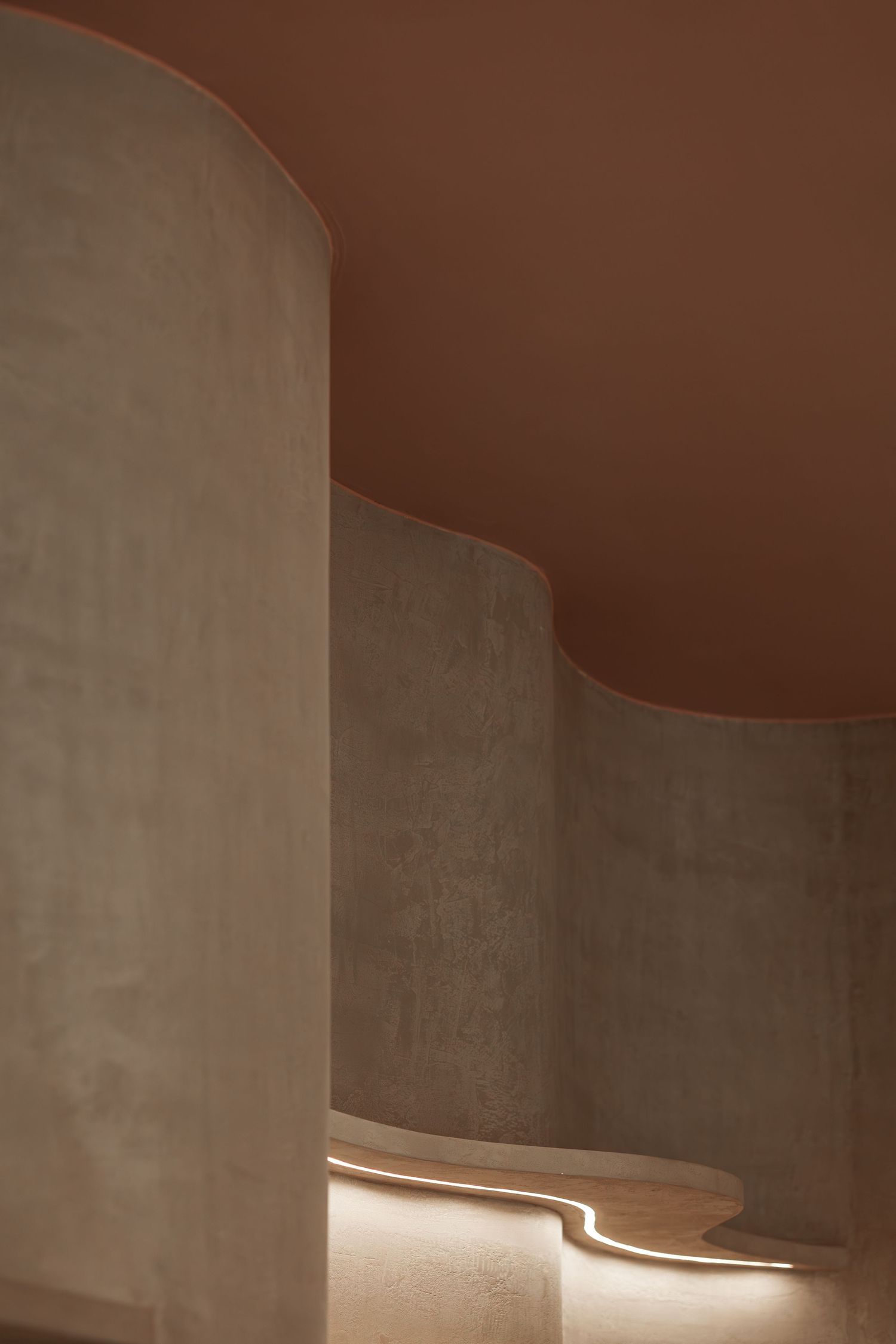Curved concrete walls with warm terracotta ceiling and subtle LED floor lighting.
