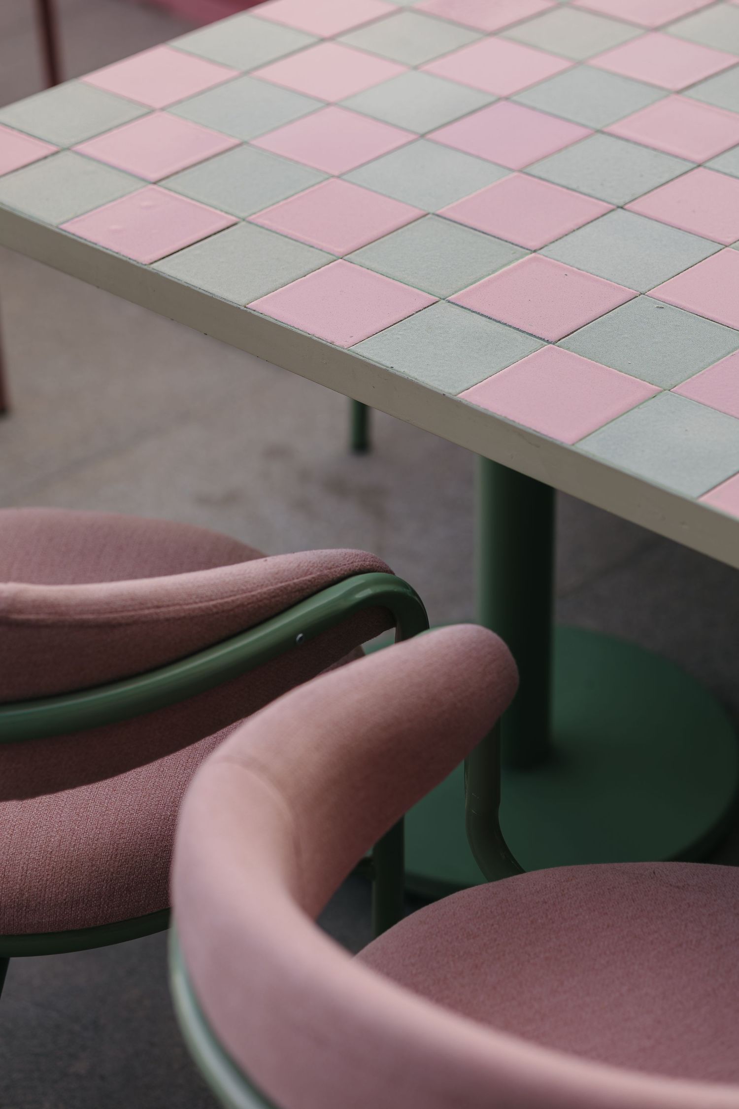 Pink upholstered chairs with green frames surrounding a checkerboard pink and green tiled cafe table.