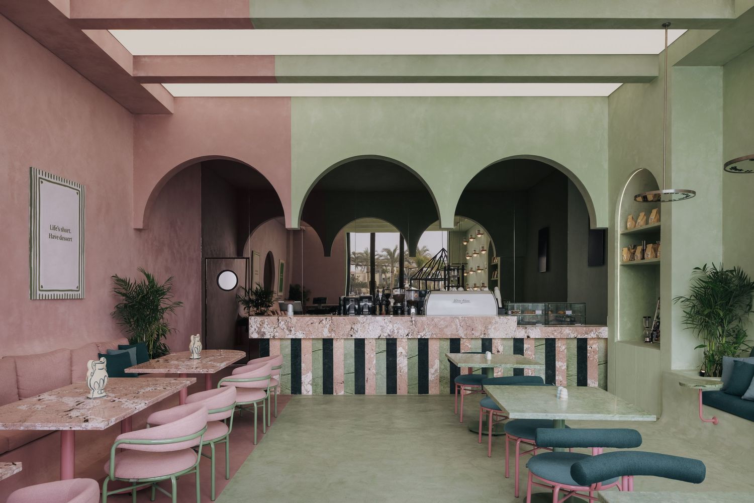 Colorful cafe interior with pink and green arched walls, terrazzo bar, and teal seating.